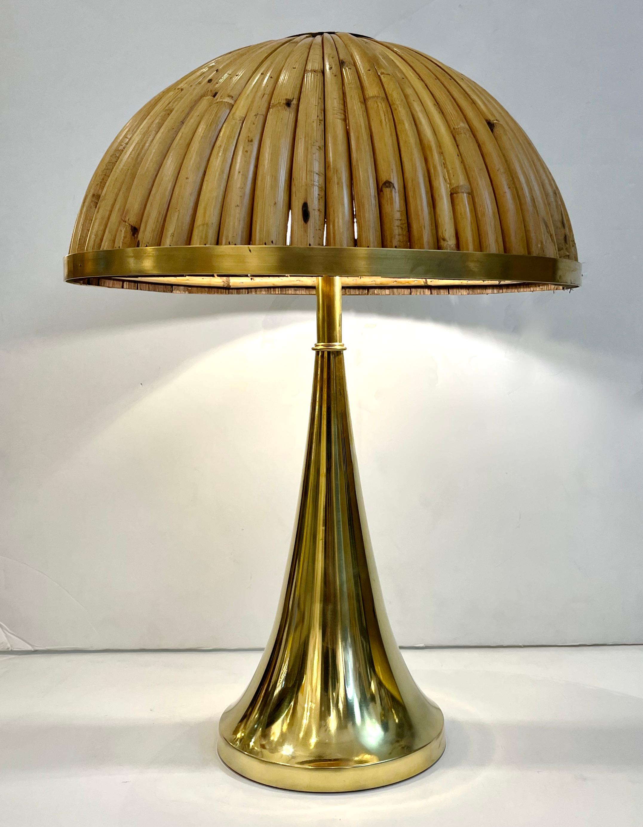 A contemporary organic modern creation, entirely handcrafted in Italy, a pair of sleek organic table lamps, the sensuous luminous brass gold body holding an elegant half moon shade entirely handmade in rattan / bamboo and made special by the edging