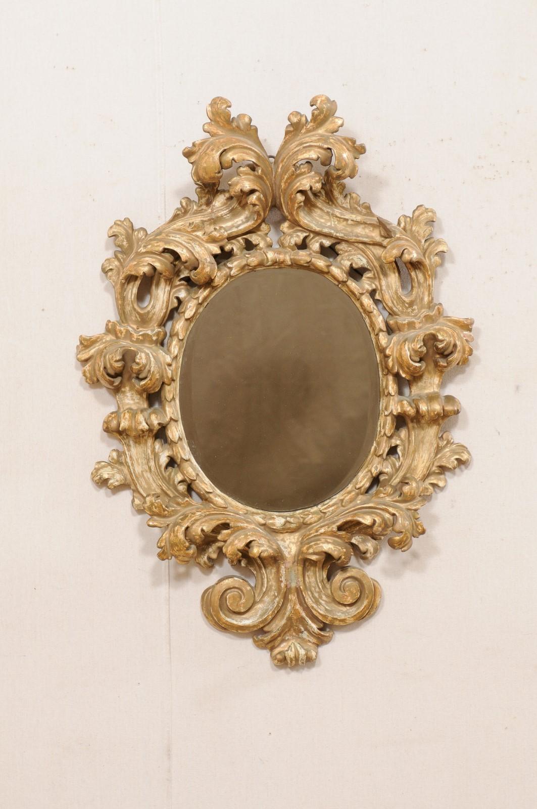An Italian carved acanthus leaf mirror from the turn of the 18th and 19th century. This elaborate antique mirror from Italy features a richly carved, ornate acanthus leaf wooden surround with oblong, oval shaped glass at center. The carved details