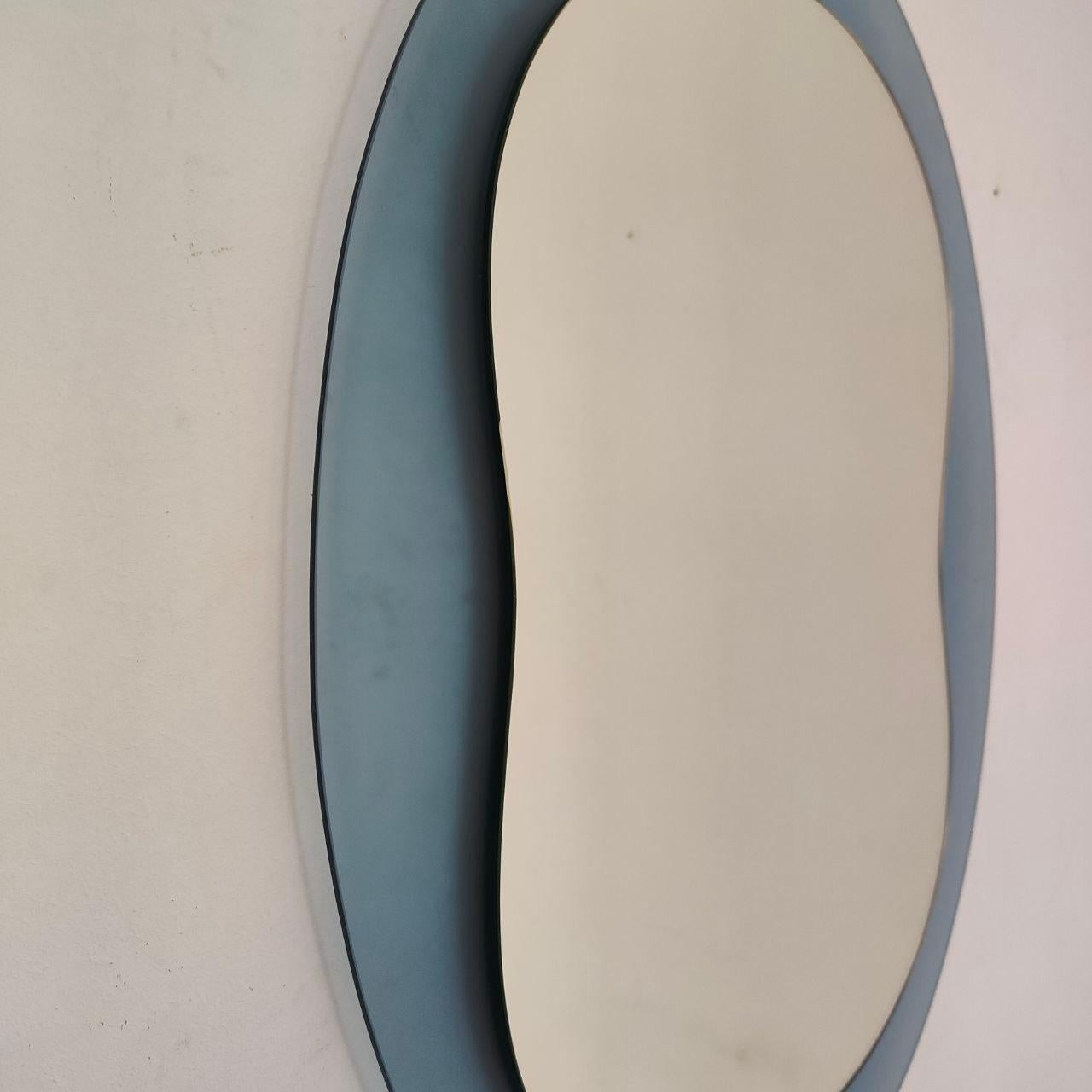 Elegant miroir mural ovale italien des années 1970, réalisé dans le style de Veca.
Cette pièce sculpturale présente une structure en verre à double couche, avec un cadre extérieur en verre teinté bleu clair et une surface intérieure en miroir,