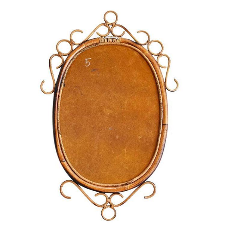 An Italian scrolled burnt bamboo and rattan wall mirror in the style of Franco Albini. The piece is oval in shape and created with a rattan and bamboo frame which surrounds the glass. The edges of the mirror are decorated with double strands of