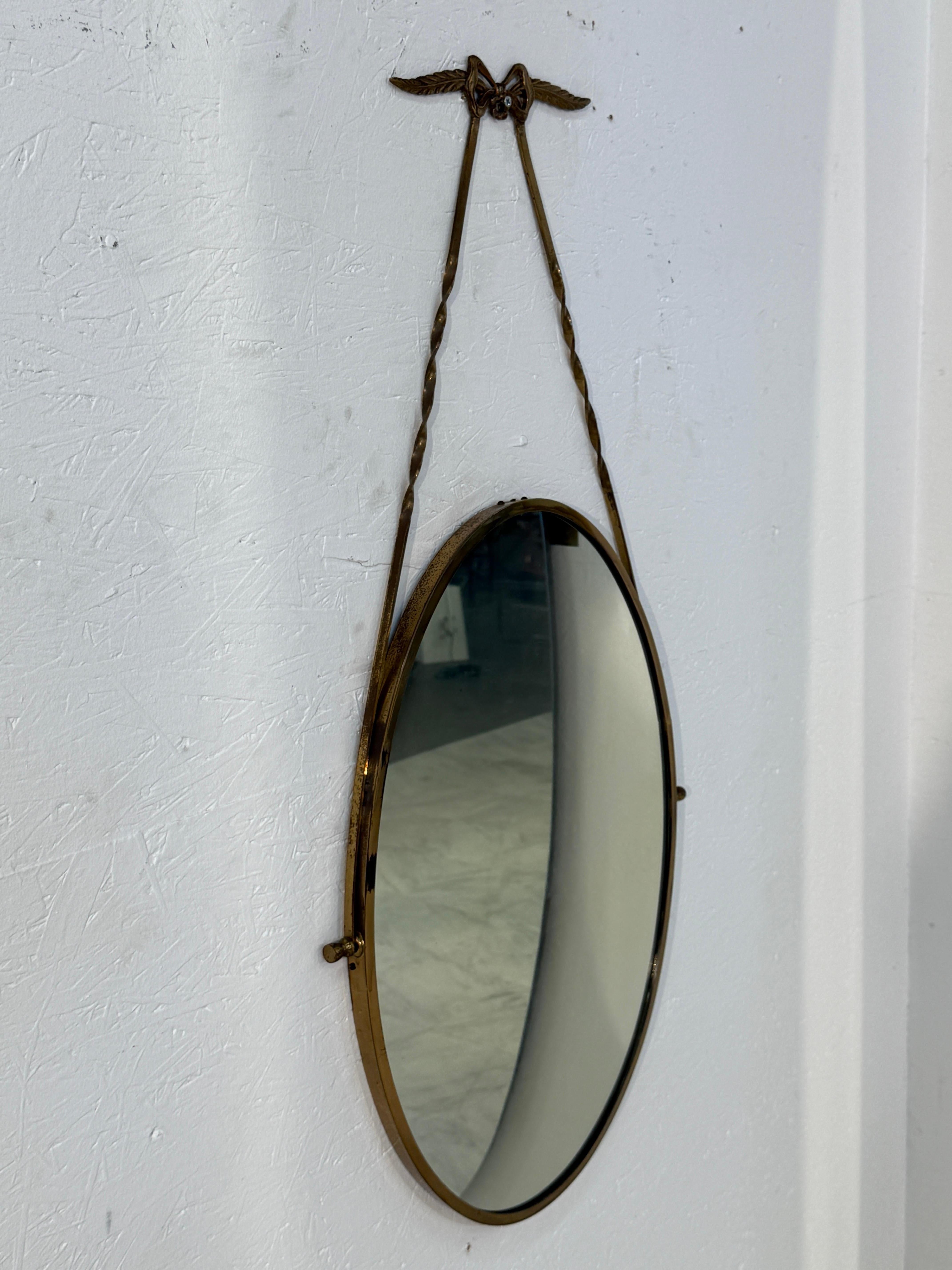 Moderno Italian oval mirror from the 1950s, featuring a brass frame suspended by a twist in vendita