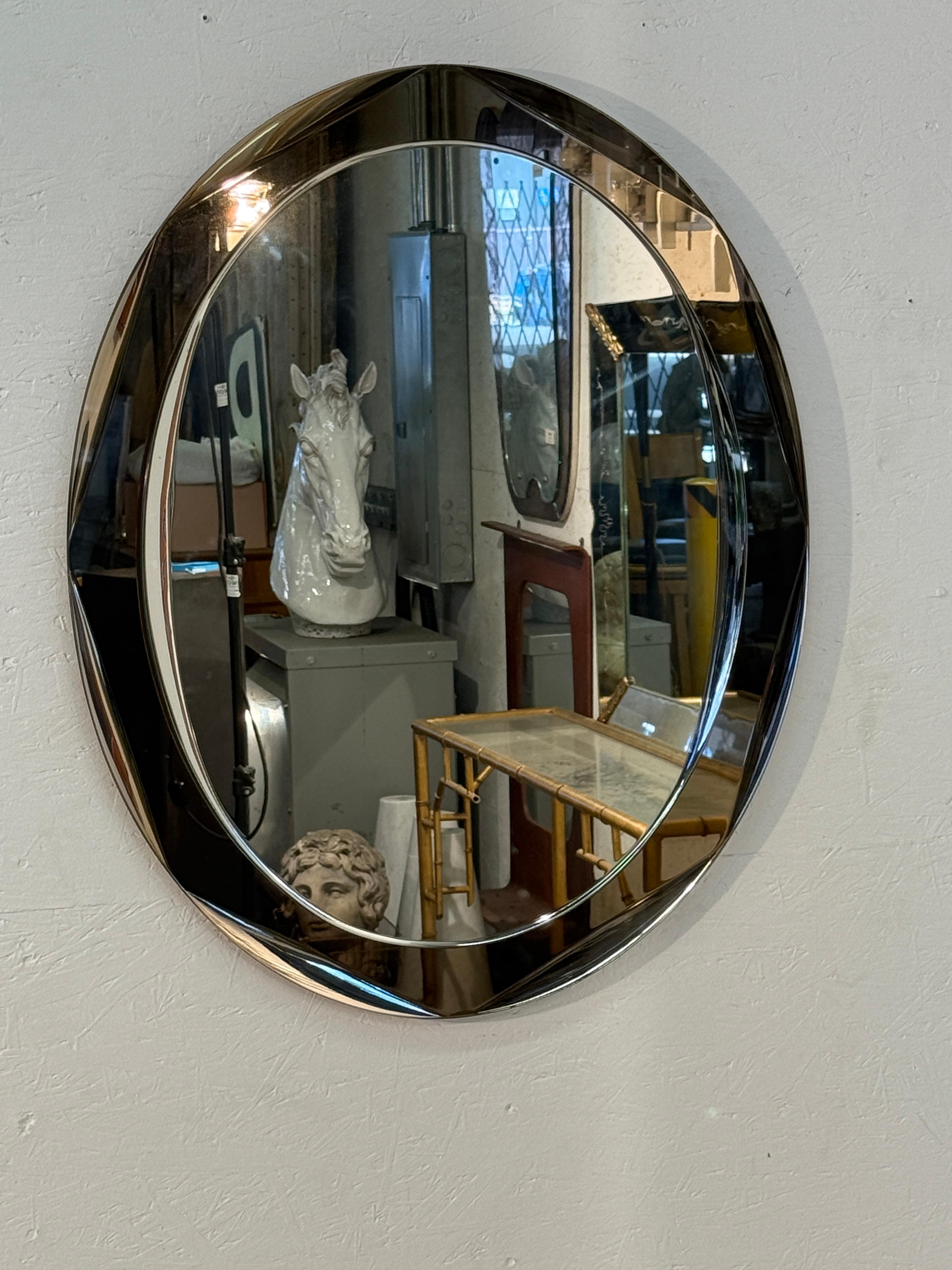Italian oval mirror from the 1970s, designed with a smoked glass border that lends depth and tonal richness to the reflective surface. The gently curved frame creates a soft, sculptural outline, enhancing the mirror’s modernist character while