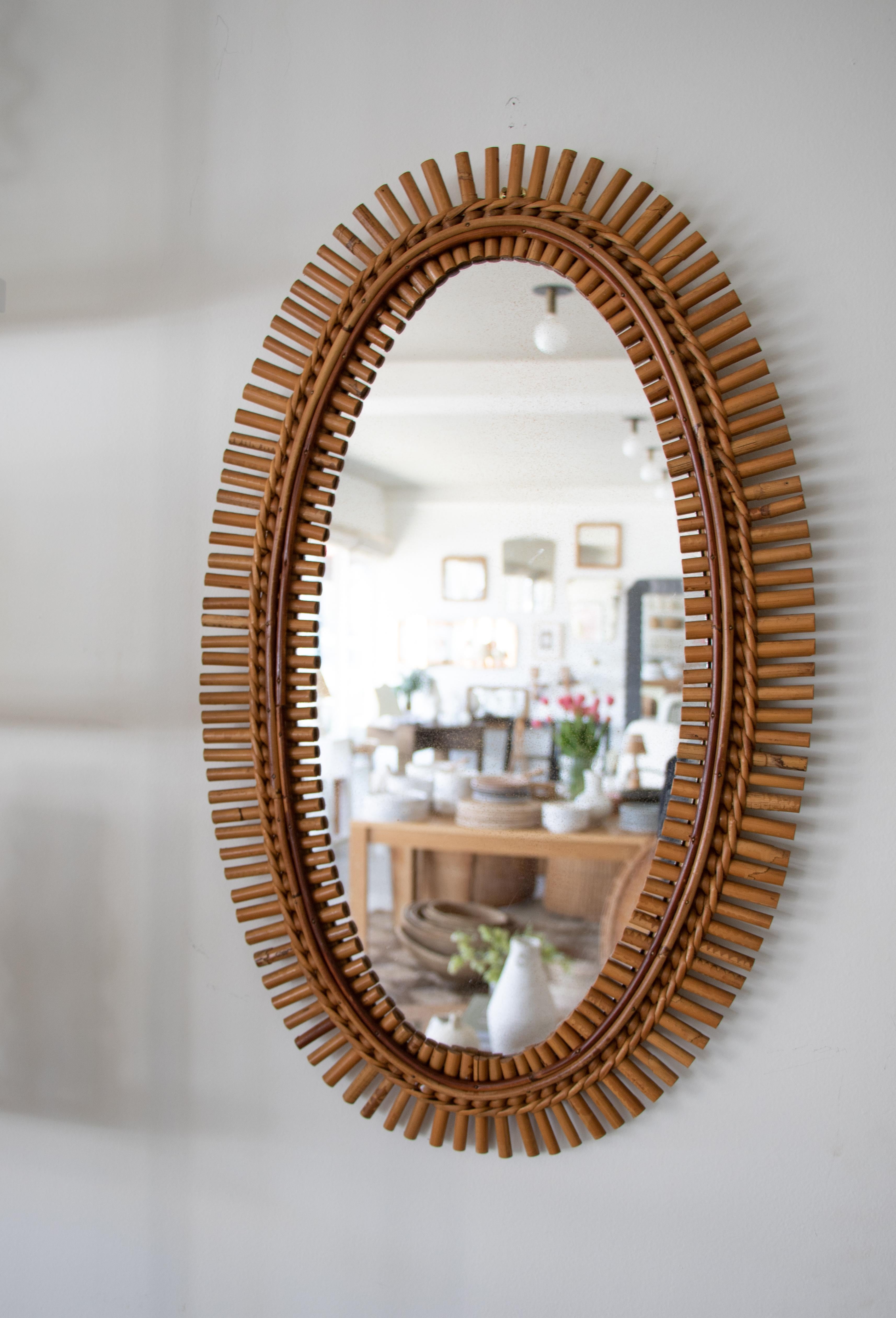 Italian rattan mirror in an oval shape with rattan encompassing the mirror. Nice vintage condition with original mirror showing age spots on mirror.