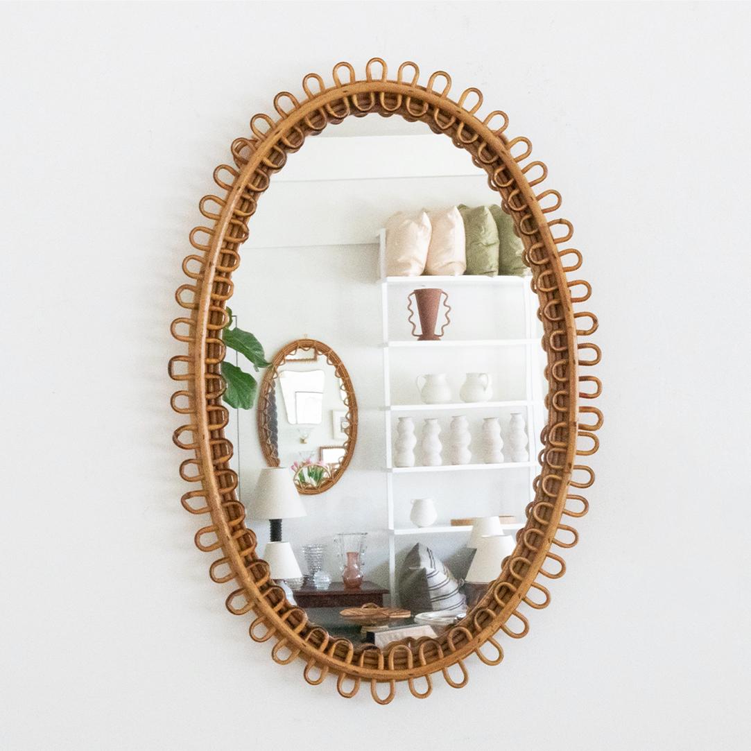 Italian rattan mirror in an oval shape with looping rattan encompassing the mirror. Nice vintage condition with original mirror showing age spots on mirror.