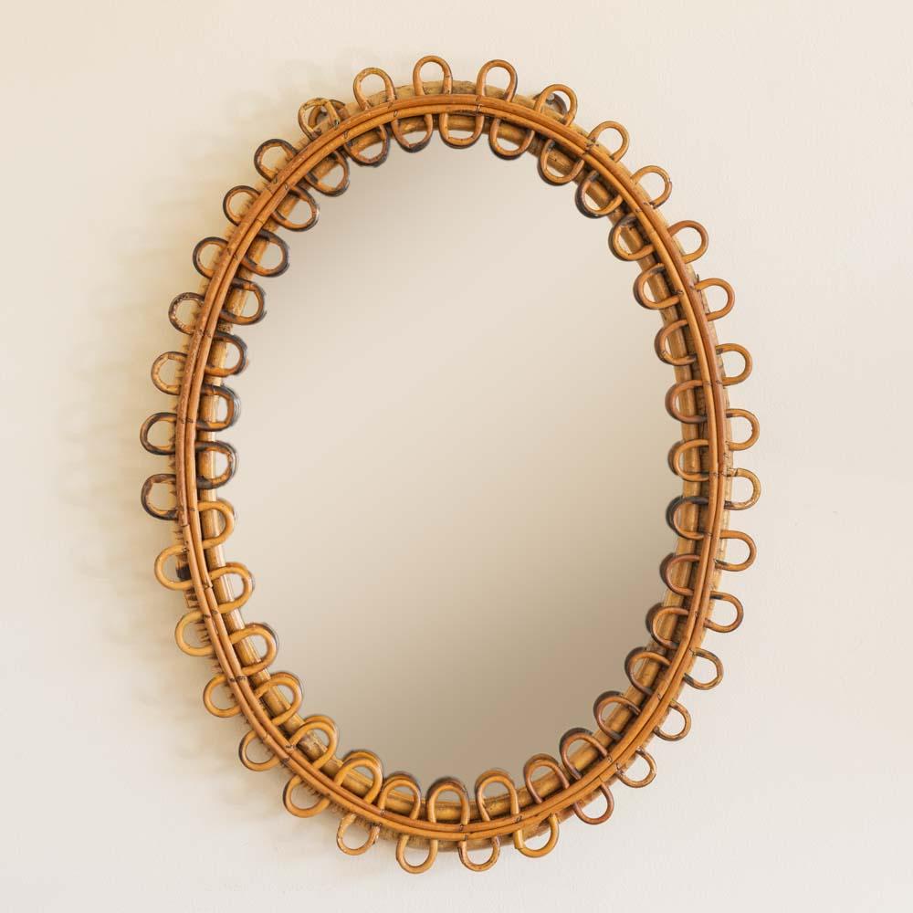 Italian rattan mirror in an oval shape with looping rattan encompassing the mirror. Nice vintage condition with original finish. Newly replaced mirror. Perfect for powder room.  