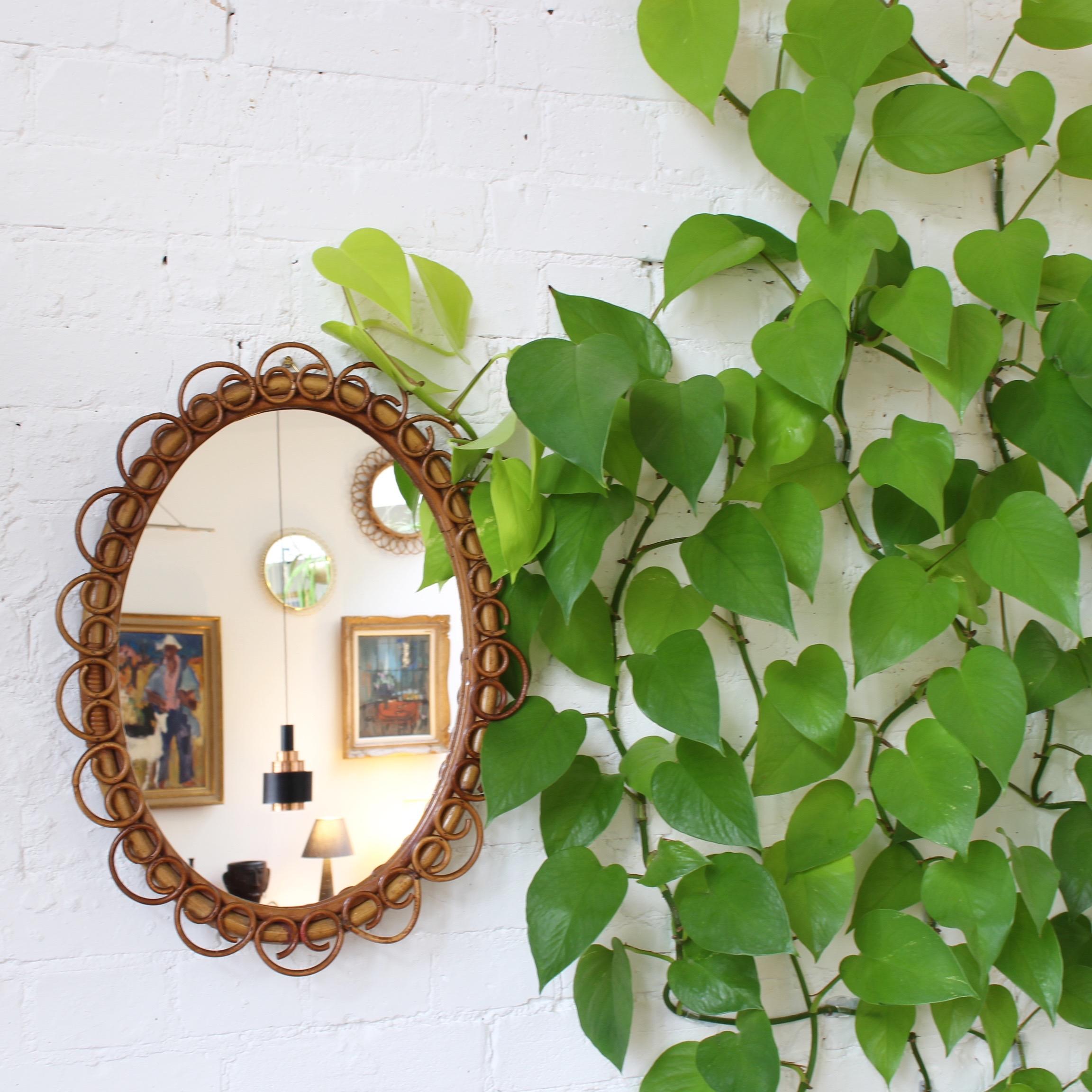 Italian oval-shaped rattan and bamboo wall mirror, circa 1960s. This mirror has a very charming oval shape with rattan pretzel-forms framing the glass. There is a characterful, aged patina on the mirror frame and many of the decorative forms. One of