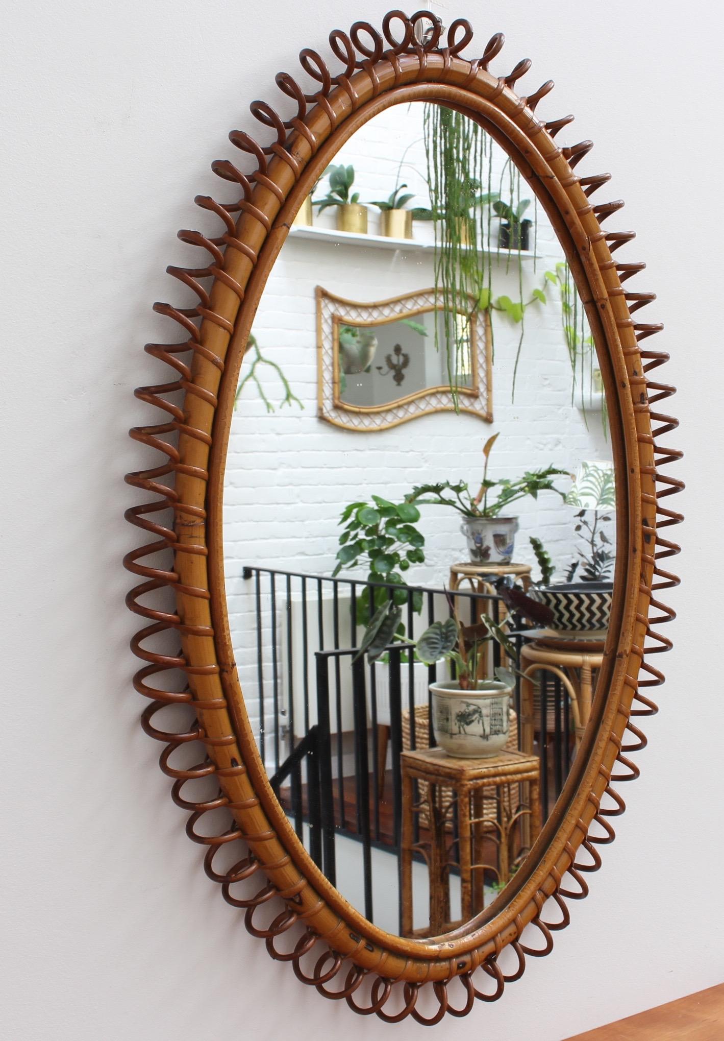 Italian rattan wall mirror (circa 1960s). This mirror has an oval form with delightful 'telephone line' shapes repeating around the rattan cane frame. The characterful, aged patina on the mirror frame attests to its age and adds to its charm. In