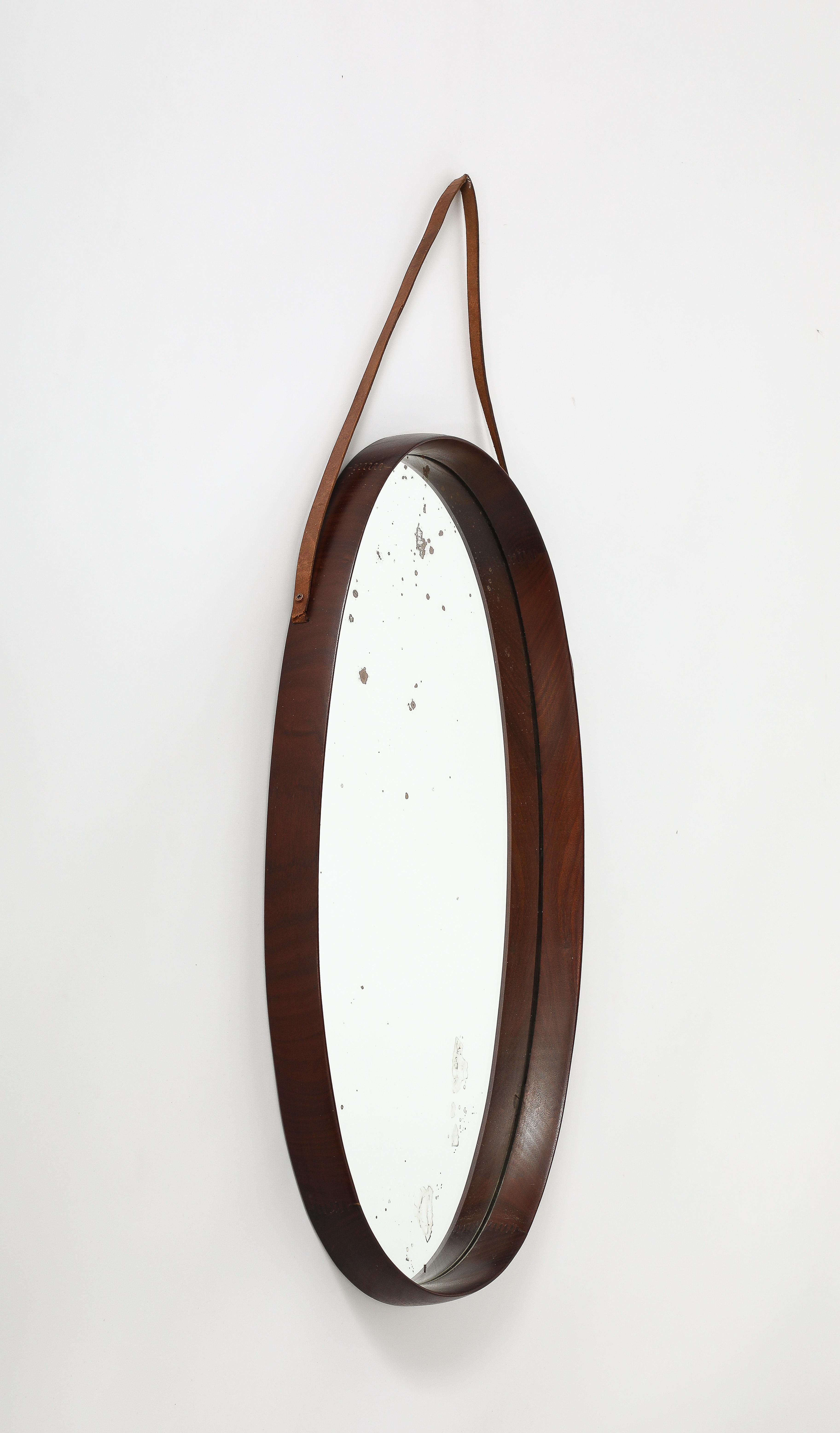An Italian oval teak wall mirror with leather strap.  A very simple and organic mid-century design.
Italy, circa 1950 
Size: 27 1/2