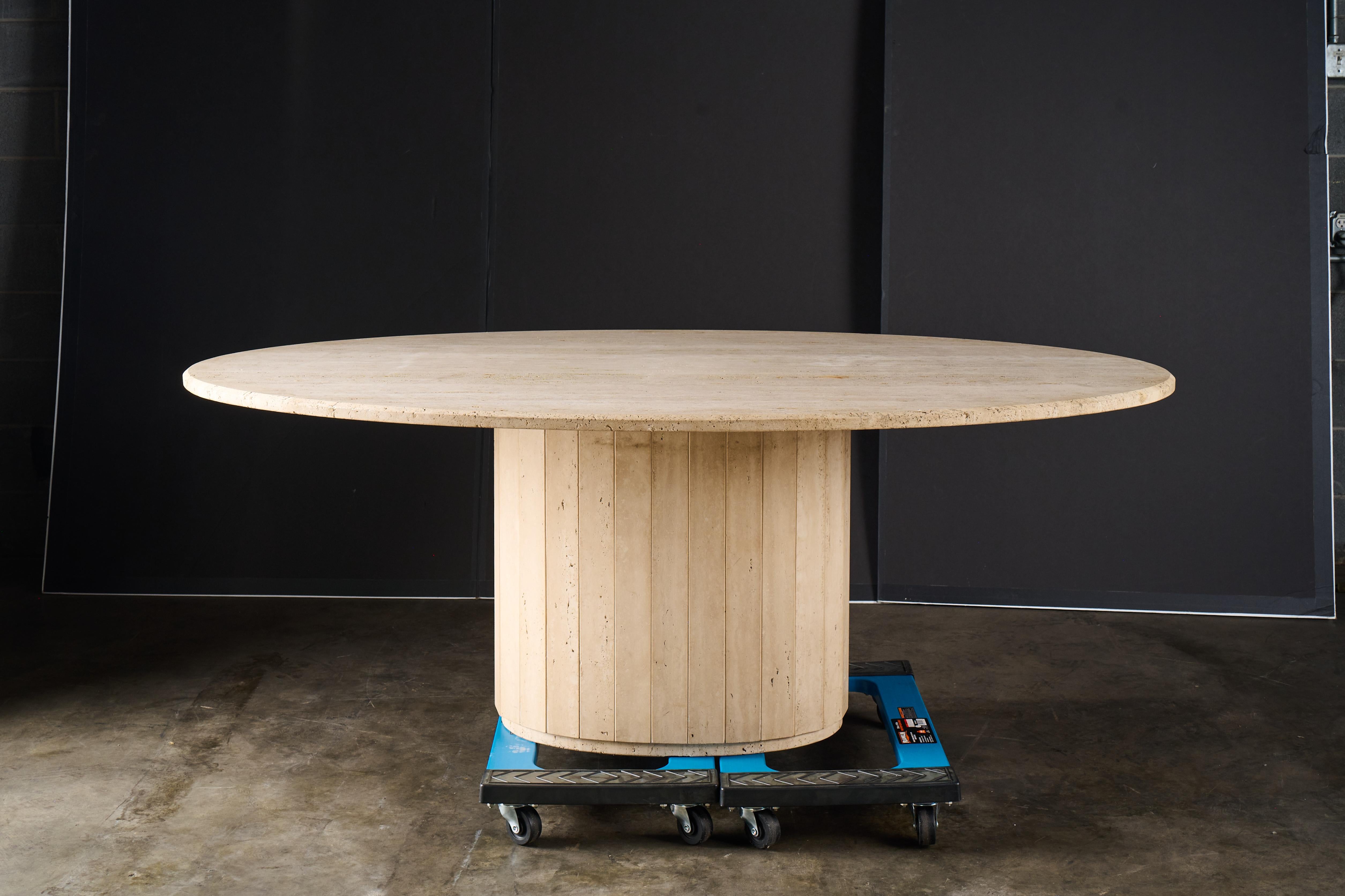 This is a vintage travertine dining table with a pedestal base, from the late 20th century. The table features an oval, smooth travertine top and a column-like base with vertical grooves, giving it a clean, minimalist design. The use of travertine