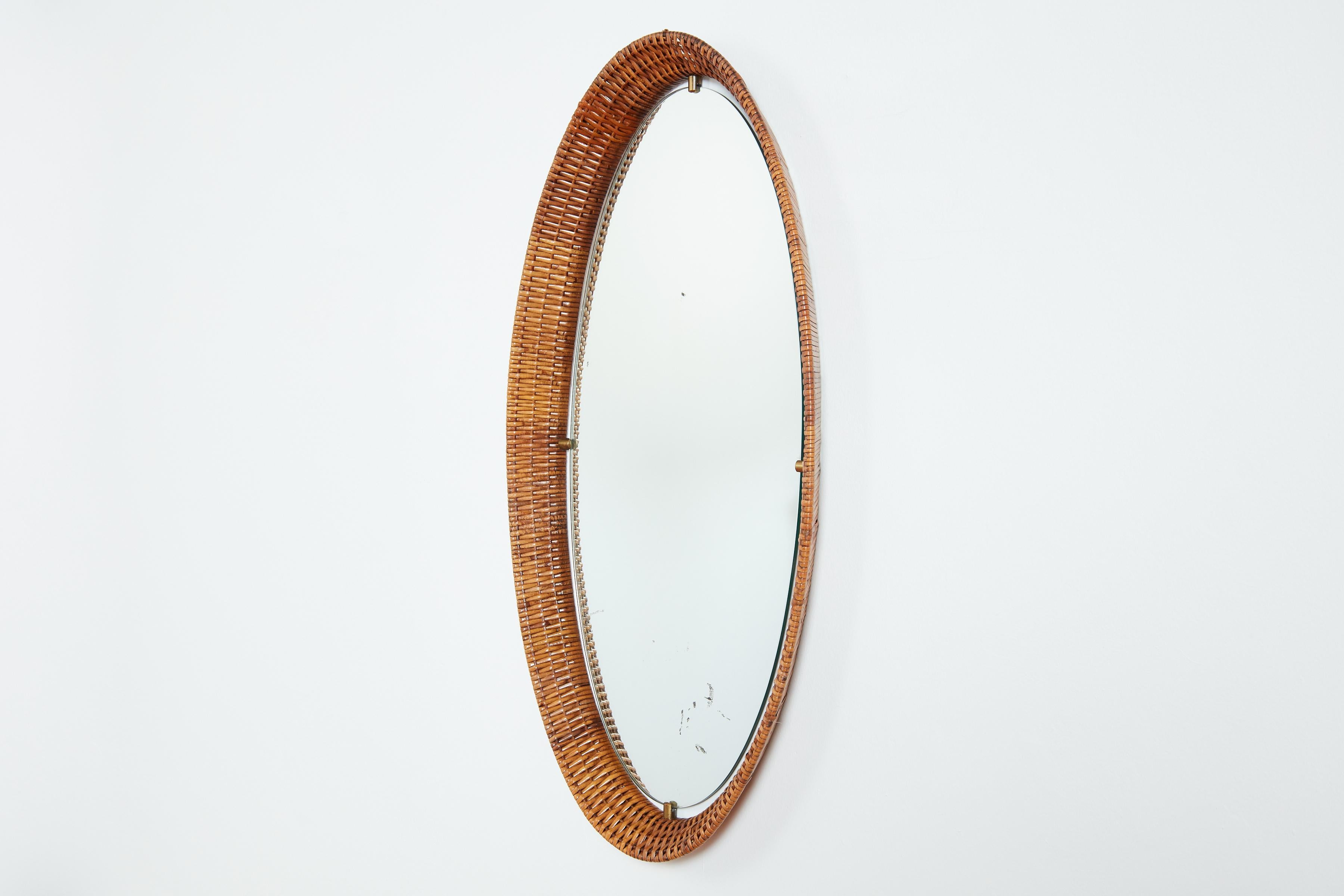 Italian woven wicker mirror in oval shape 
Brass clasp hardware with floating mirror 
Great patina to original mirror - which can be replaced with new mirror upon request.
Italy, 1950s