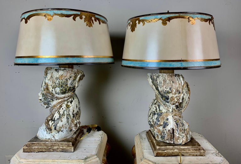 A pair of custom lamps made with 19th century painted and parcel-gilt carved columns mounted into table lamps and crowned with hand painted parchment shades that coordinate perfectly with the antique elements.