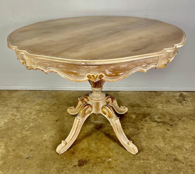 Charming Italian painted & parcel gilt dining table. Most of the paint has worn away but there are beautiful remnants of gold leaf throughout. The table has a center pedestal that sits on four legs detailed with carved acanthus leaves. The top has a