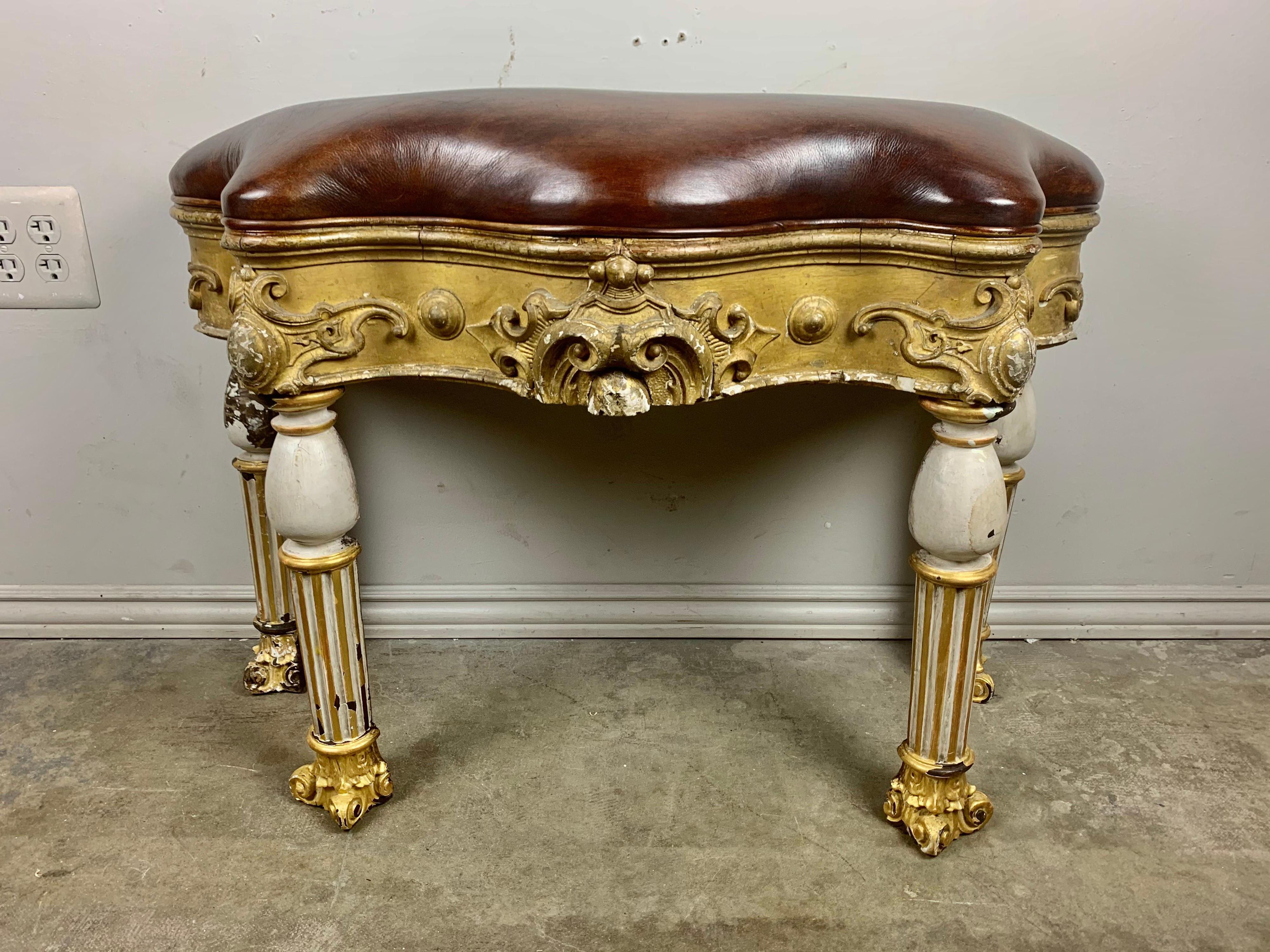 Custom serpentine shaped bench made with antique Italian painted and parcel gilt fluted legs with capital feet. The bench is newly upholstered in chestnut colored leather with self cord detail.