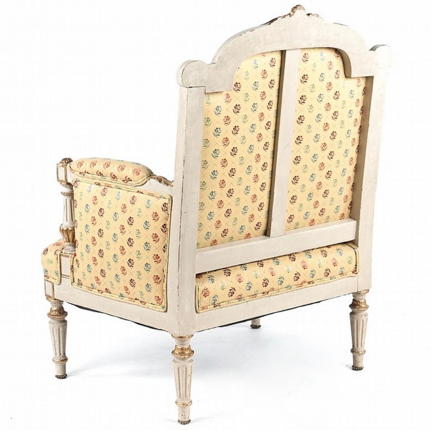 A charming ca. 1850 cream and gilt armchair of generous proportions, on tapered fluted legs, and with upright fluted baluster armrests in the Louis XVI manner. The back is arched with gilded scroll terminals to the crest rail, embellished with a