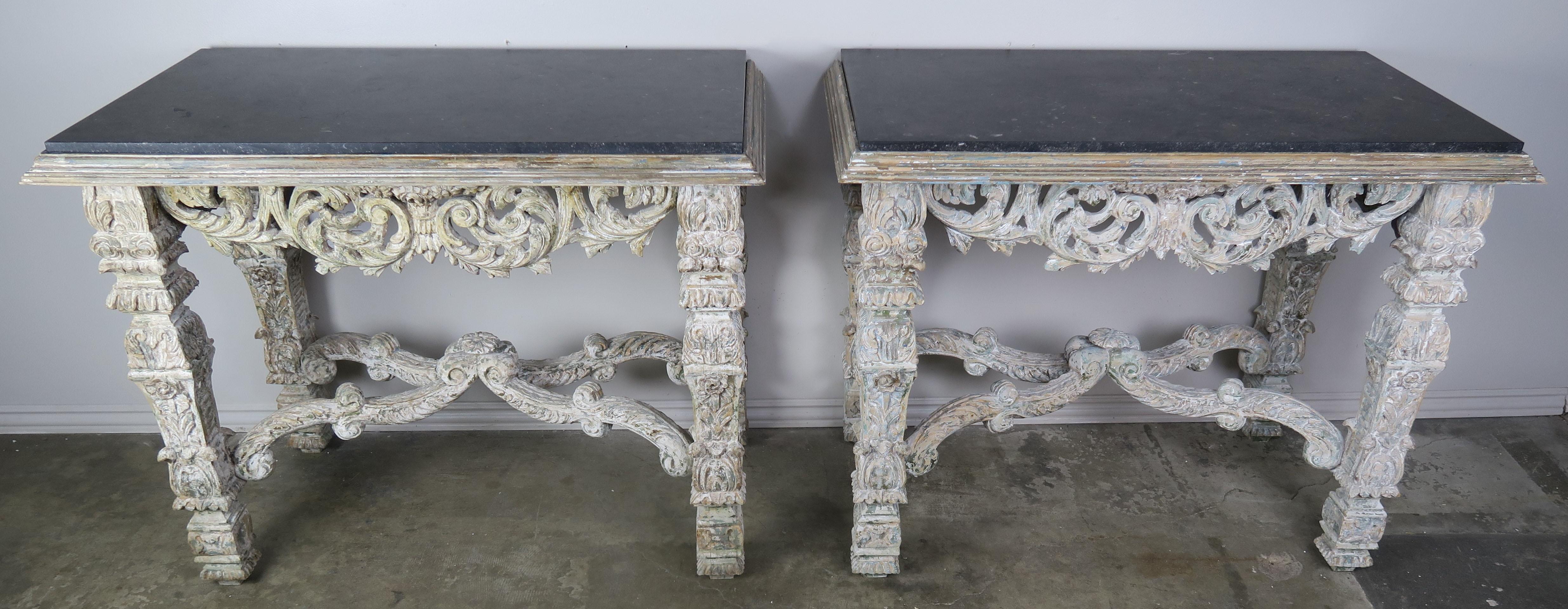 Pair of Italian Baroque style painted consoles beautifully hand-carved with swirling acanthus leaves, flowers, and various patterns throughout. The tables stand on four heavily carved straight legs that are connected by a center stretcher. Inset
