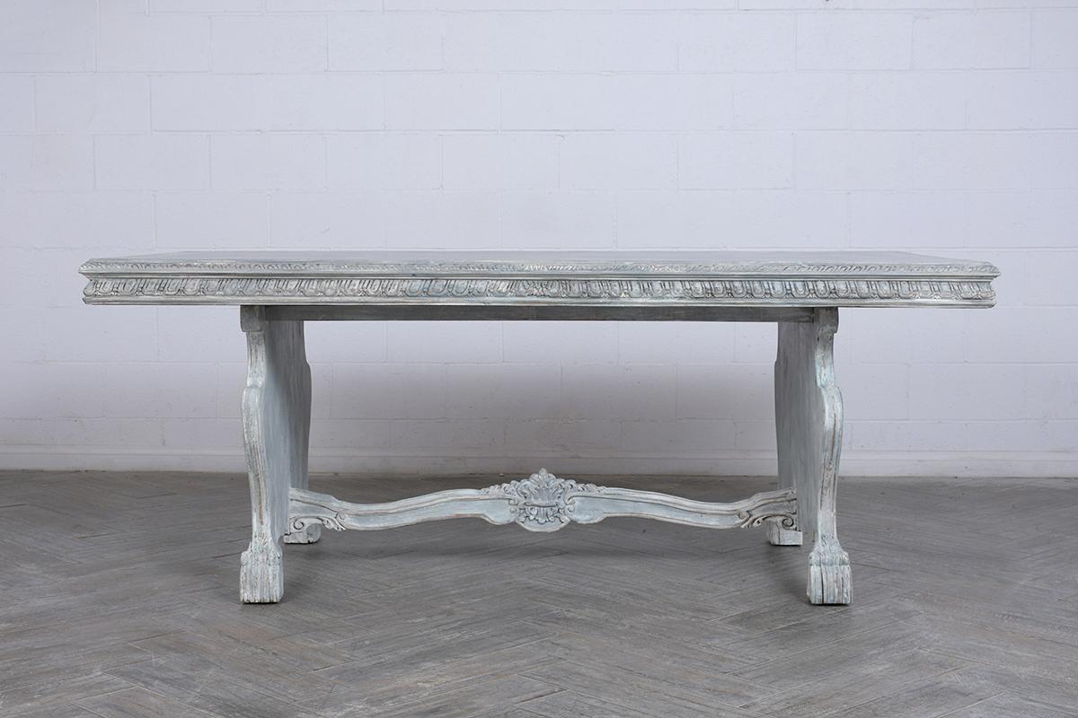 This Antique Italian Baroque Dining Table is made out of wood newly painted a pale gray-blue & off white color with a distressed finish and is fully restored. This writing table features a wooden top with detailed moldings, heavily carved wood