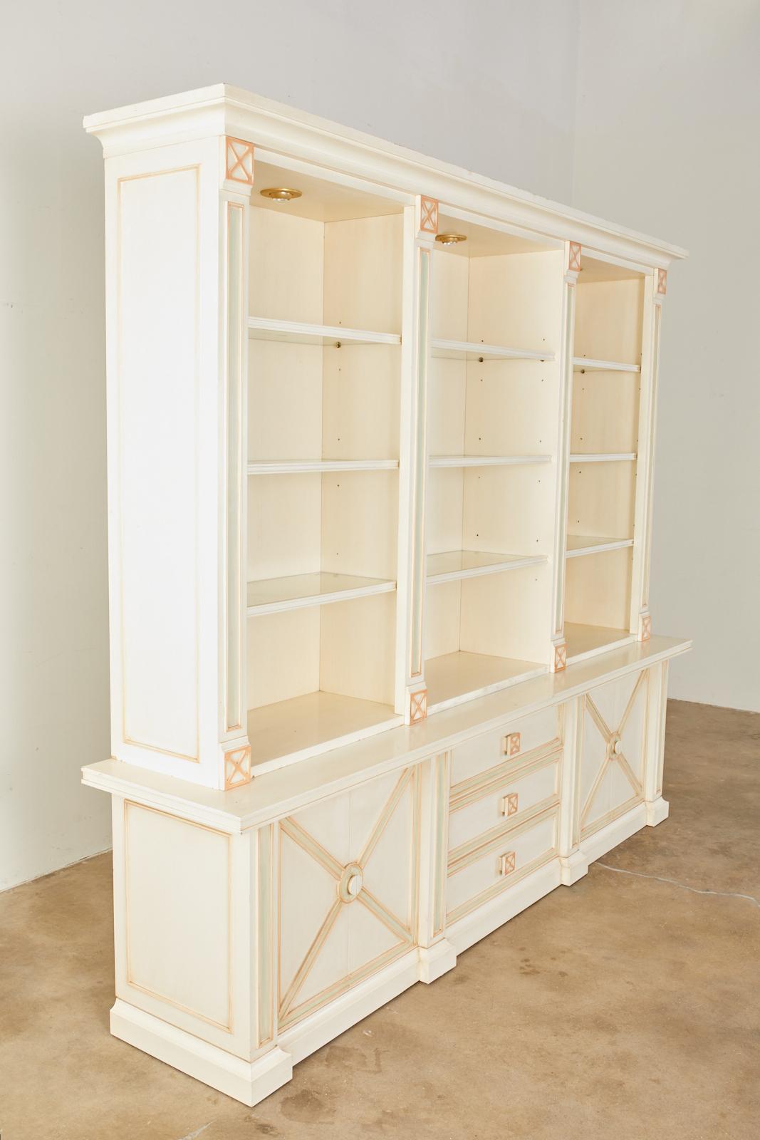 Large late 20th century Italian two-part bookcase cabinet featuring a painted finish with a neoclassical motif. The top of the case is fitted with nine glass shelves with adjustable height brackets. The corniced top has small brass finished lights