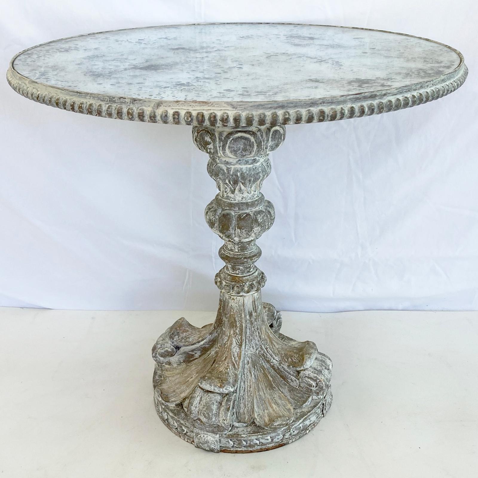 Occasional table, having a round top of antiqued mirrorplate, inset on painted table base, having a reeded border, raised on a knopped, pedestal base, carved with scrolls, beading, and acanthus details, ending in a round foot. 

Stock ID: D3952.