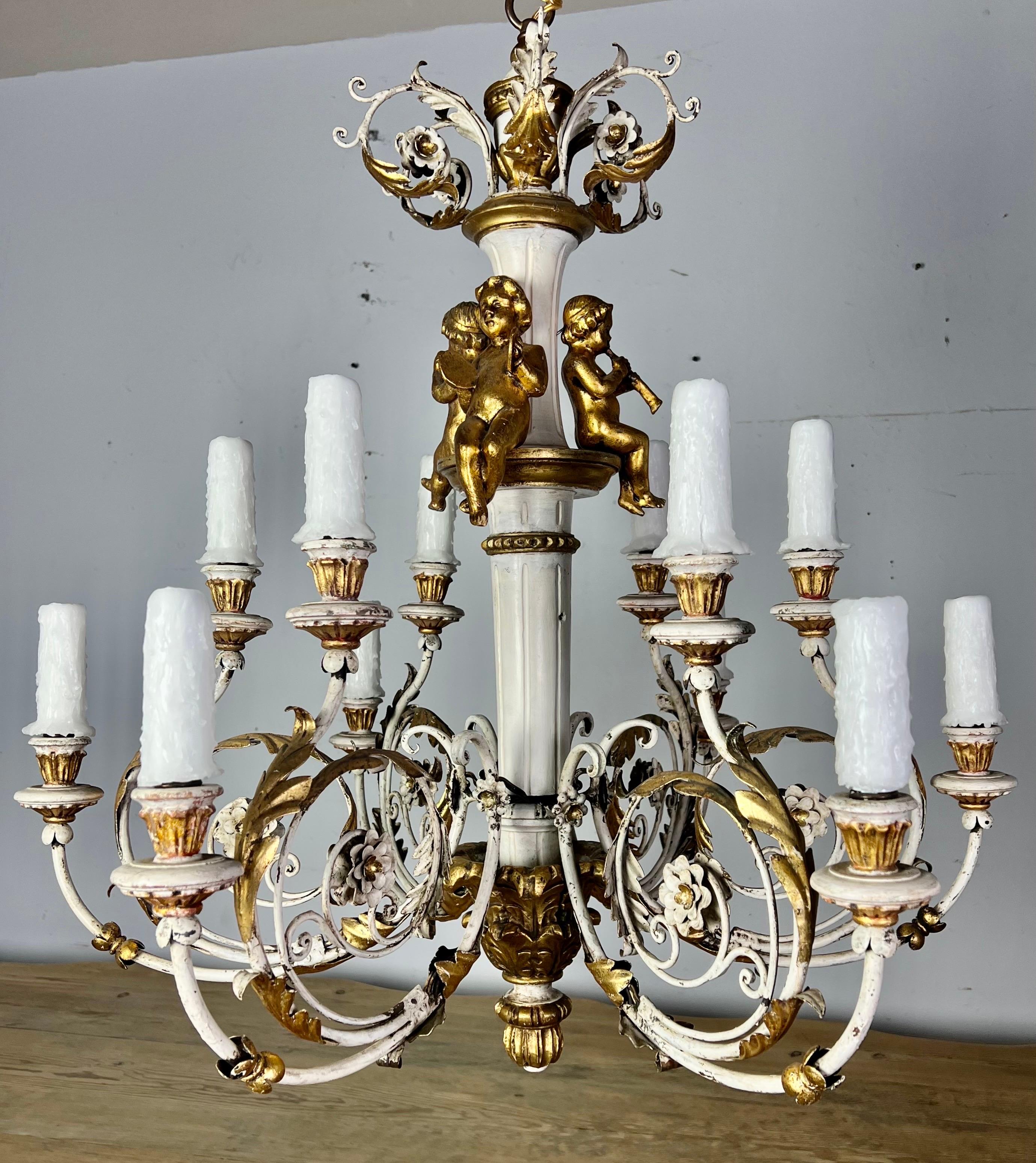 Italian twelve light painted & parcel gilt Rococo style chandelier with carved wood cherubs. The fixture is made of iron & wood and includes three giltwood cherubs playing musical instruments. The chandelier has been rewired with drip wax candles.