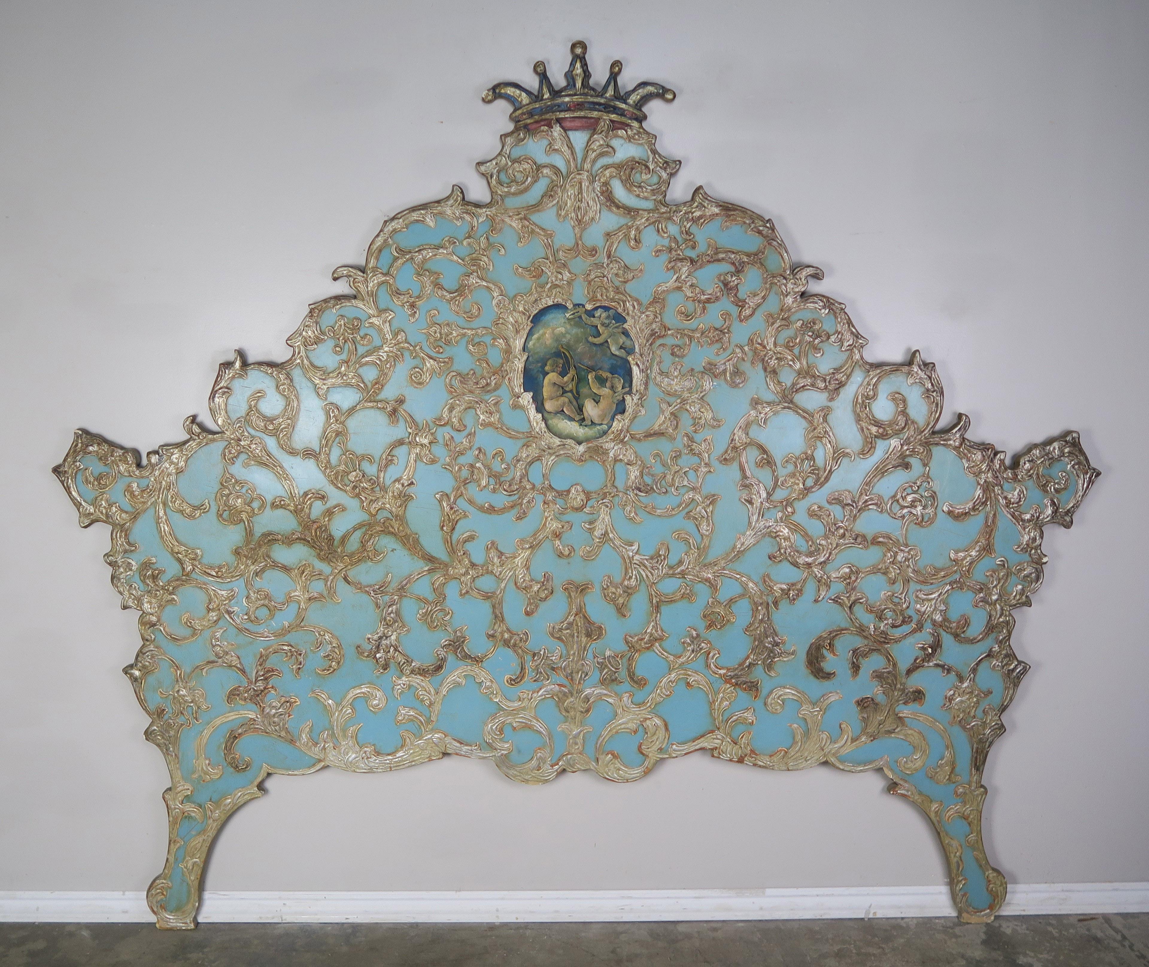 Italian 1930s blue painted headboard with raised gilt acanthus leaf design throughout. Beautiful fine painted puttis in center cartouche. Crown depicted at top of headboard as well.