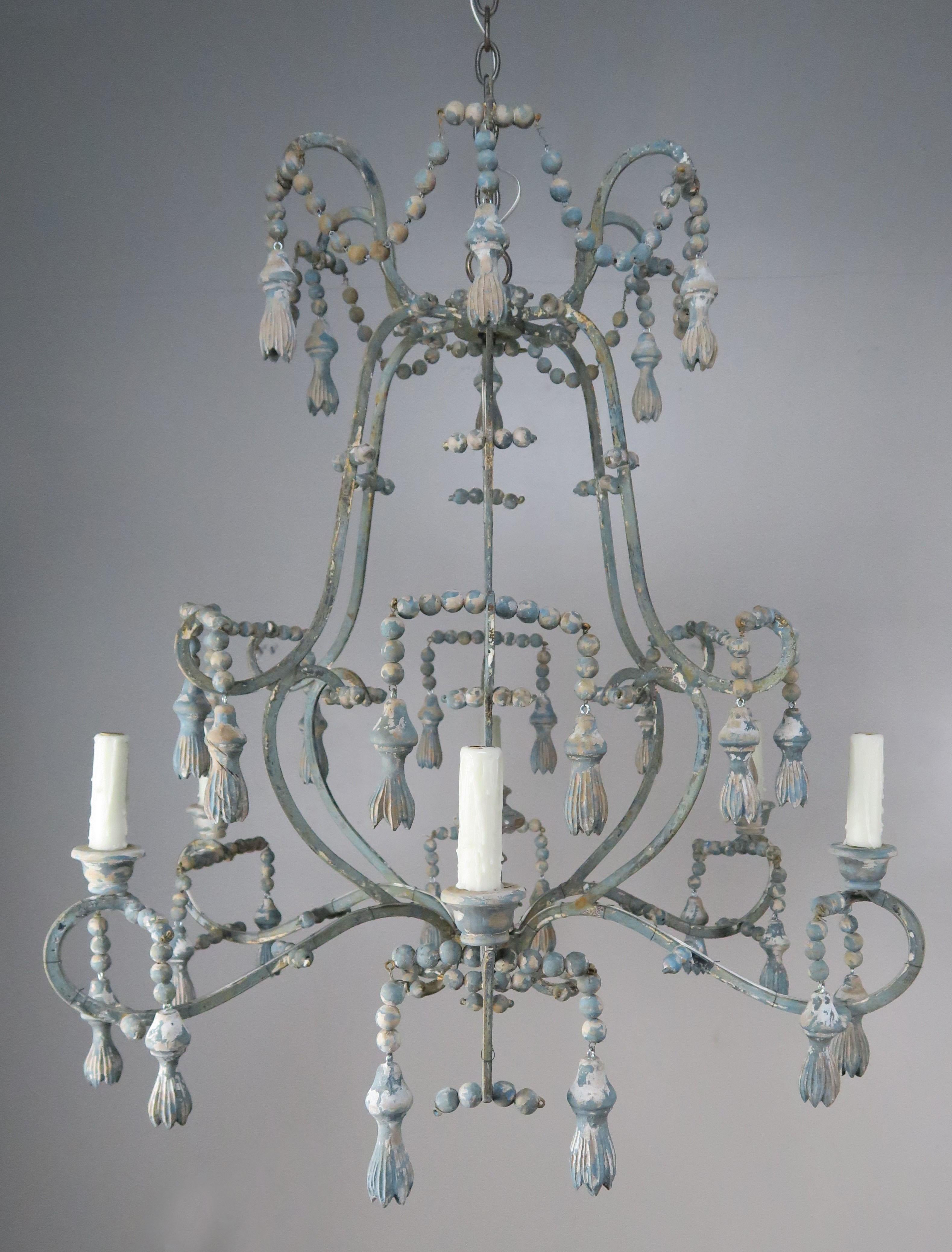 Italian style painted six-light wrought iron chandelier with wooden tassels, beads, bobeches and centre giltwood finial. The fixture is newly rewired with drip wax candle covers and includes chain and canopy. The finish is beautifully distressed