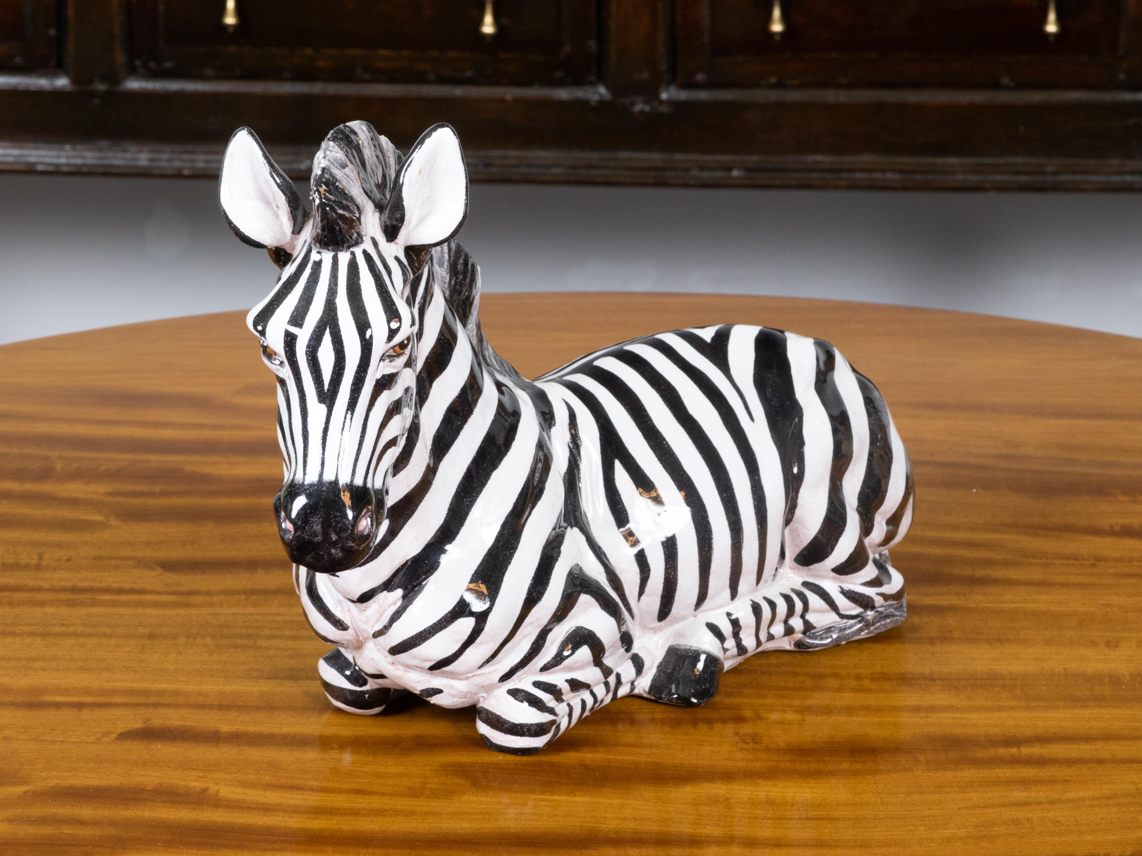 Eine kleine italienische handbemalte Terrakotta-Tierskulptur, die ein auf dem Boden liegendes Zebra mit braunen Augen darstellt. Diese im 20. Jahrhundert in Italien geschaffene, bemalte Terrakotta-Skulptur bezaubert mit der zarten Darstellung eines