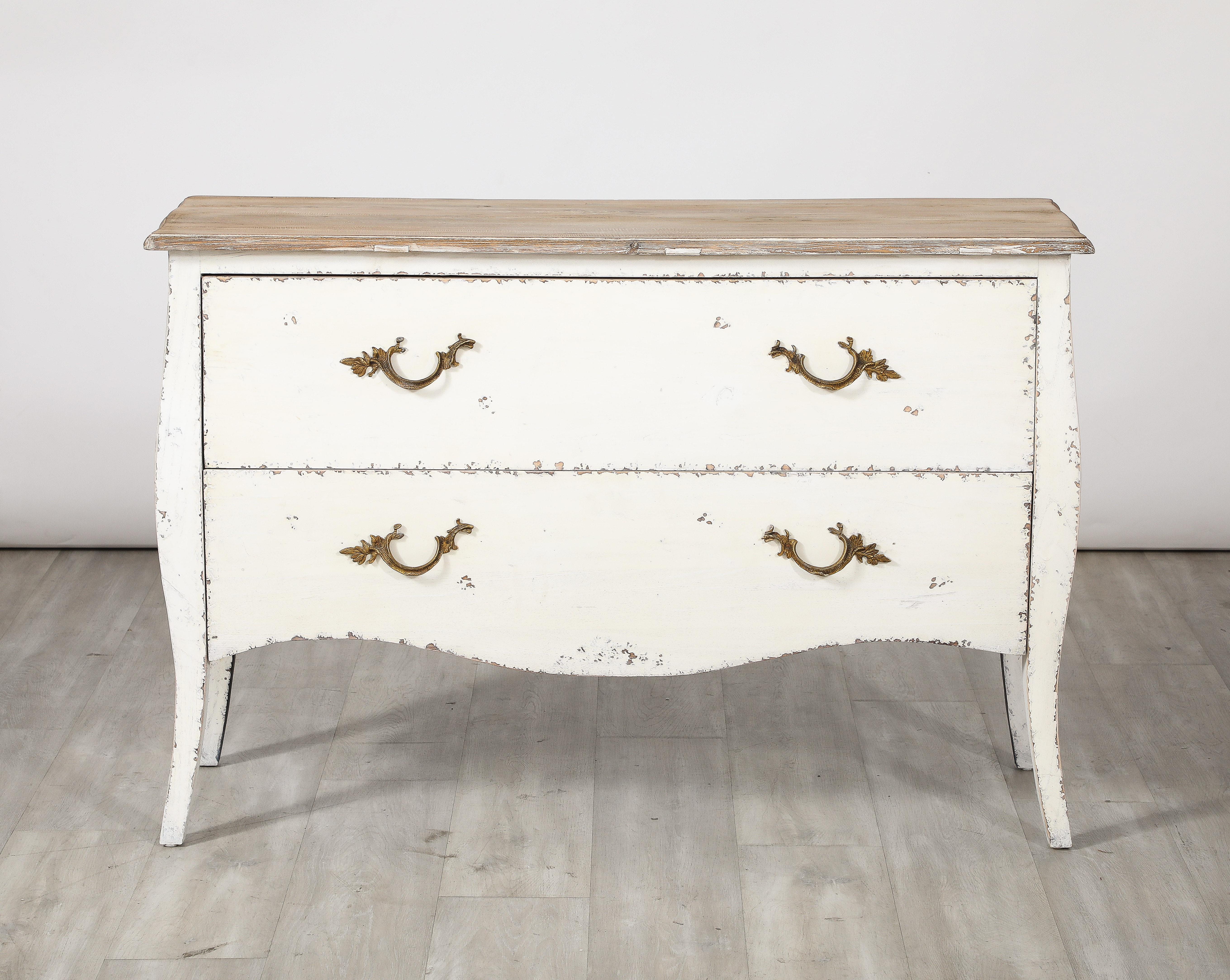 An Italian Rococo manner painted white commode.  The shapely chest comprises two-drawers with fanciful bronze handles supported on cabriole legs.   An exuberant and elegant shape which contrasts nicely with the creamy white painted finish, making it