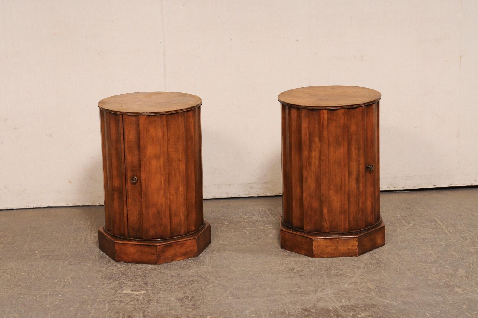 An Italian pair of column-style wooden side cabinets with round marble tops. These vintage tables from Italy have round marble tops that rest upon a wooden case which has been designed in an rounded vertical column style, with single door that opens