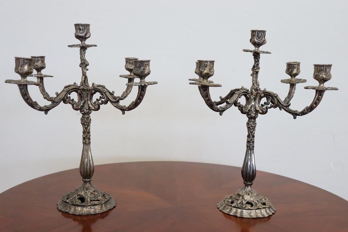 Ti presentiamo questa coppia di candelieri a 5 bracci in metallo argentato realizzati in Italia nella seconda metà del XX secolo. Caratterizzato da una linea classica che richiama uno stile antico con una decorazione ricca di riccioli e