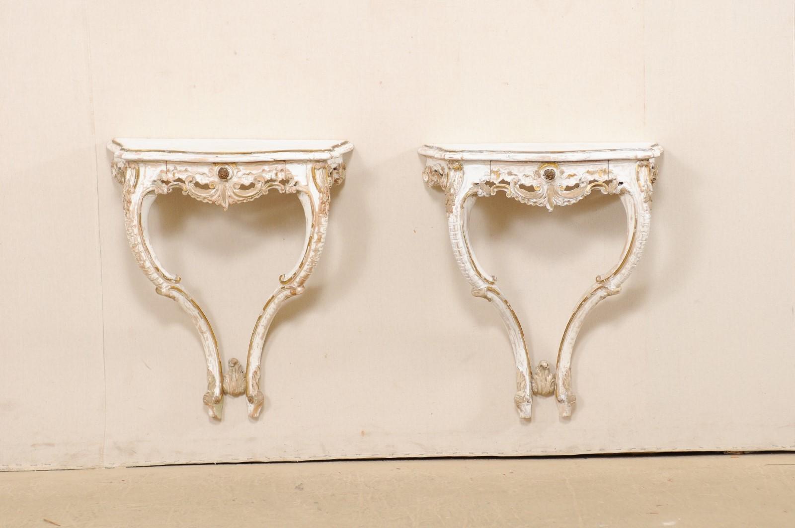 An Italian pair of carved-wood wall mounted console tables from the mid-20th century. This vintage pair of tables from Italy each feature a beautifully scalloped edge top above an elaborately pierce-carved wood skirt (which houses a single drawer at
