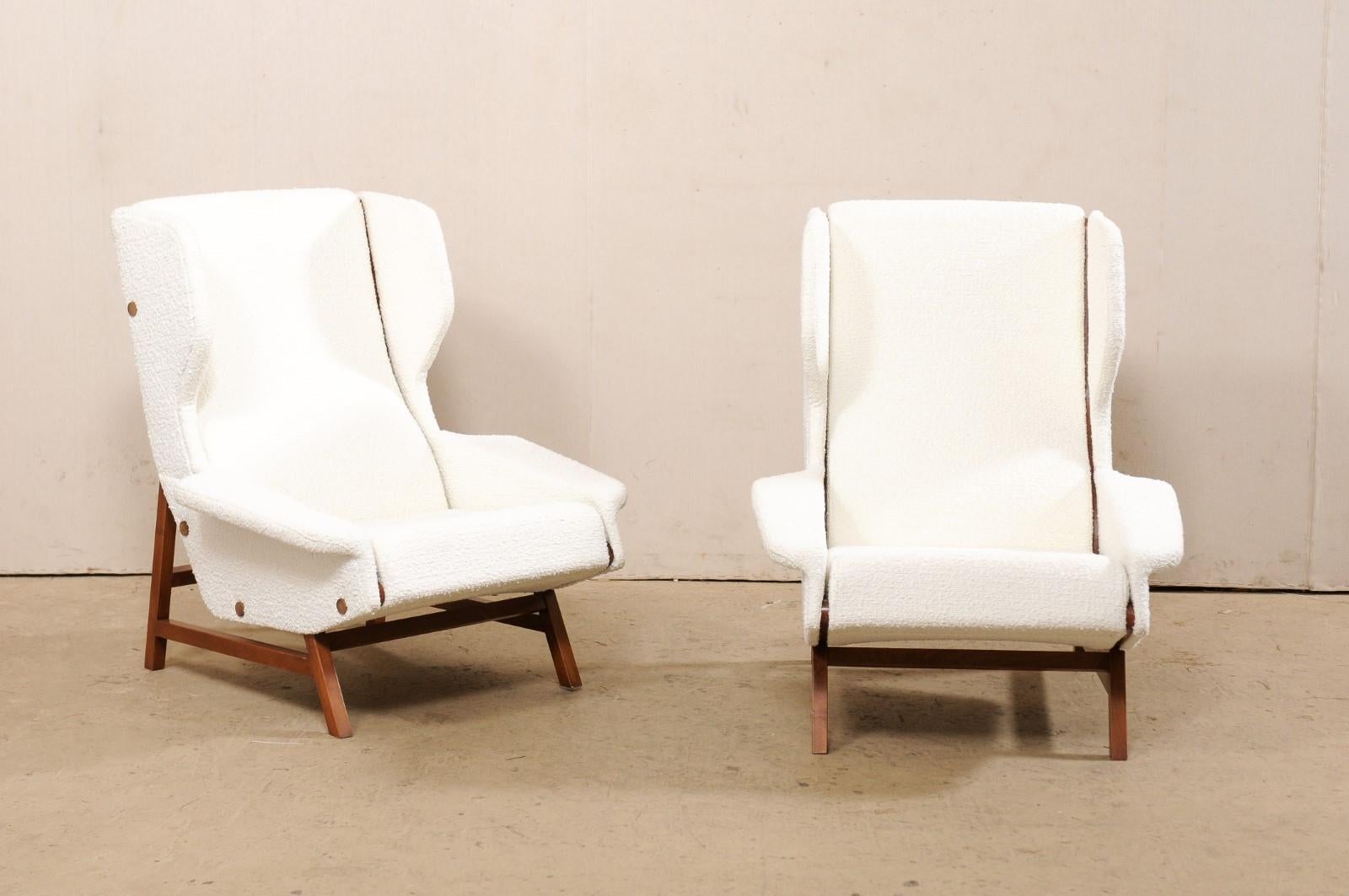 An Italian pair of nicely-sized and modern-designed upholstered wingback chairs in white. This pair of mid-century inspired club chairs from Italy each feature tall, tilted, rectangular backs with forward facing wings at top, generously oversized