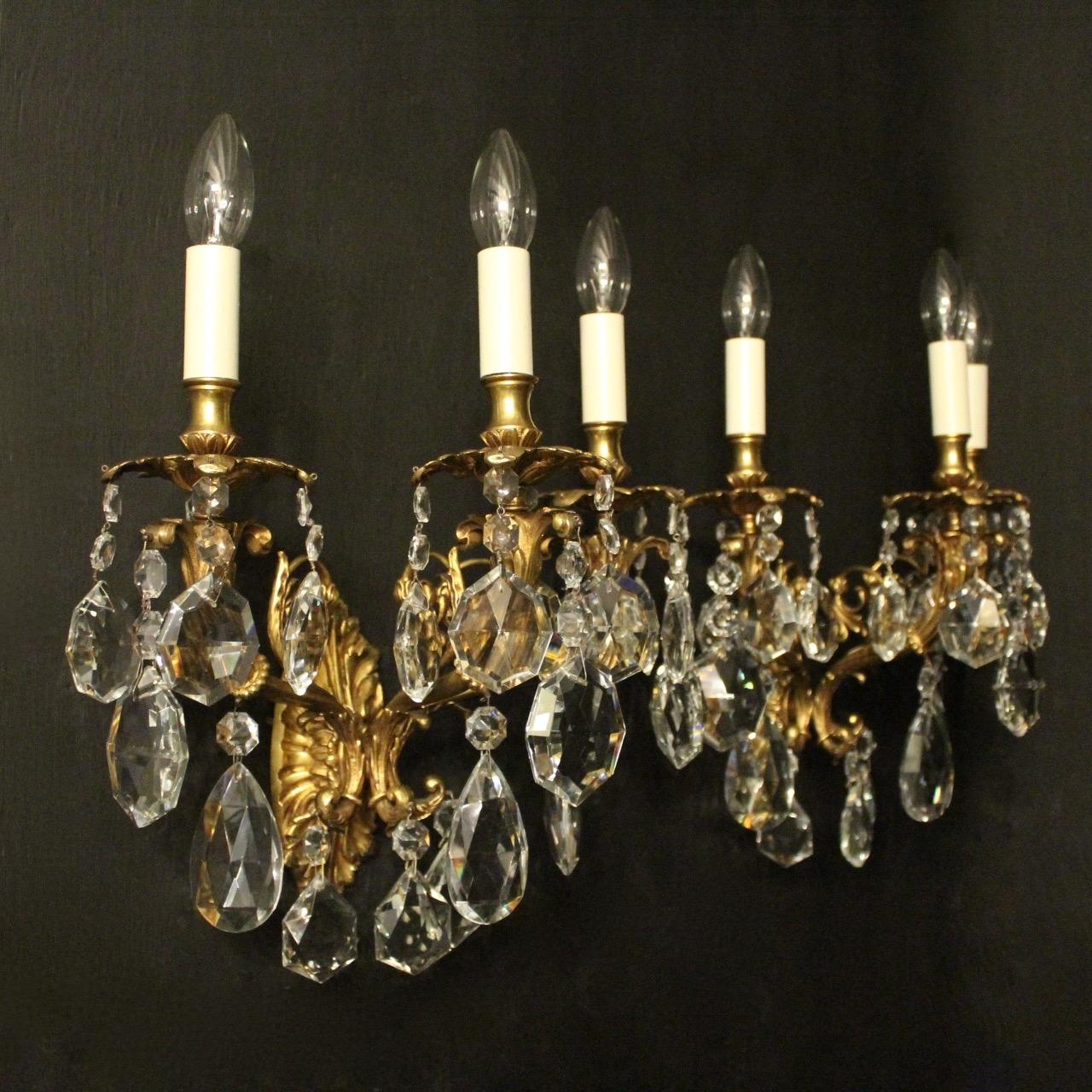 An Italian pair of gilded bronze and crystal triple arm antique wall lights, the leaf scrolling arms with leaf bobeche drip pans and bulbous leaf candle sconces, issuing from a foliated oval backplate and decorated overall with quality cut-glass