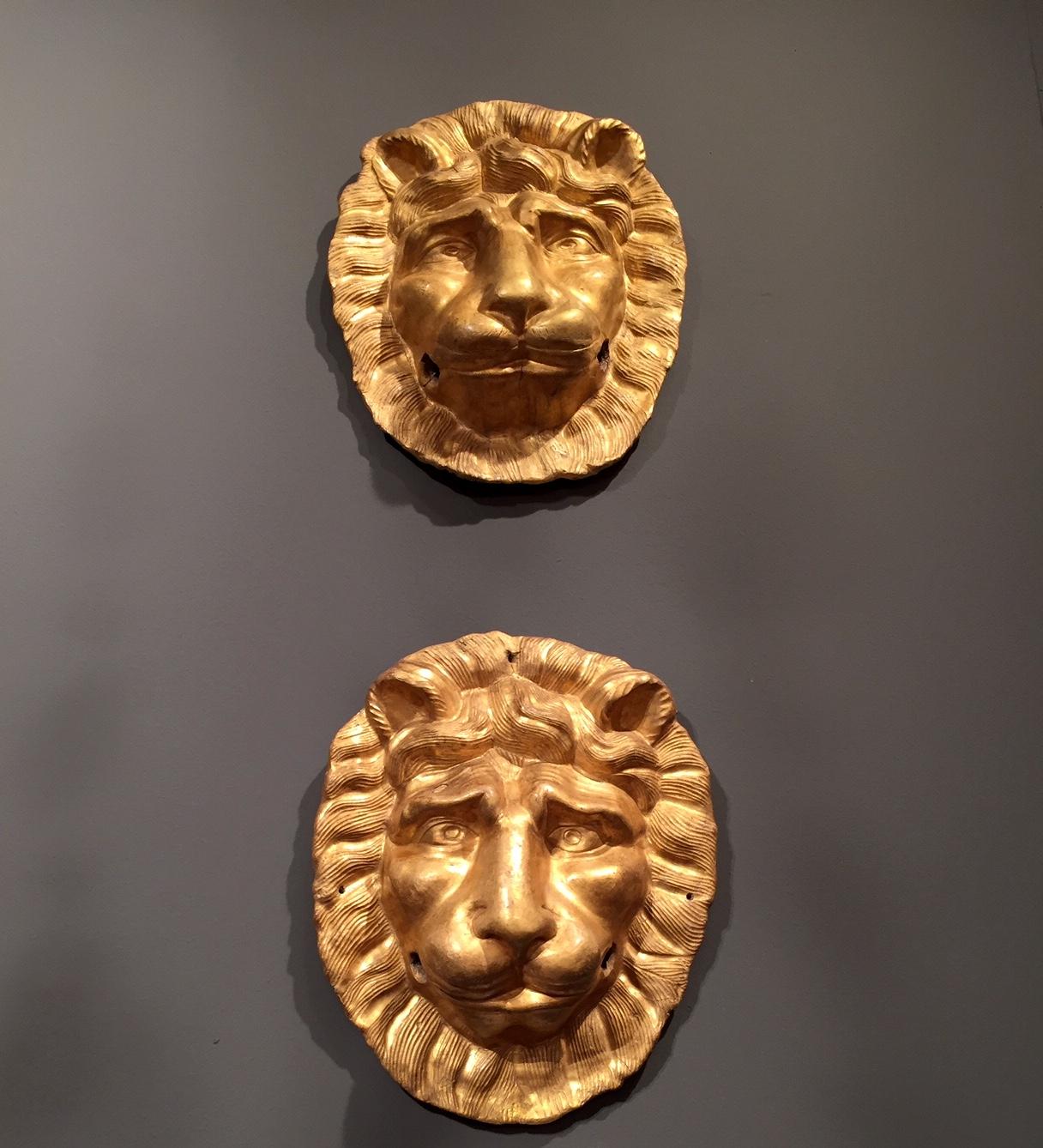 Pair of 19th century Italian gilded lion head papier-mâché masks, a pair of antique furniture ornamental elements. This pair of antique gilded sculptures, handcrafted in papier mâché, depicting two heads of lions are inspired to the masks of ancient