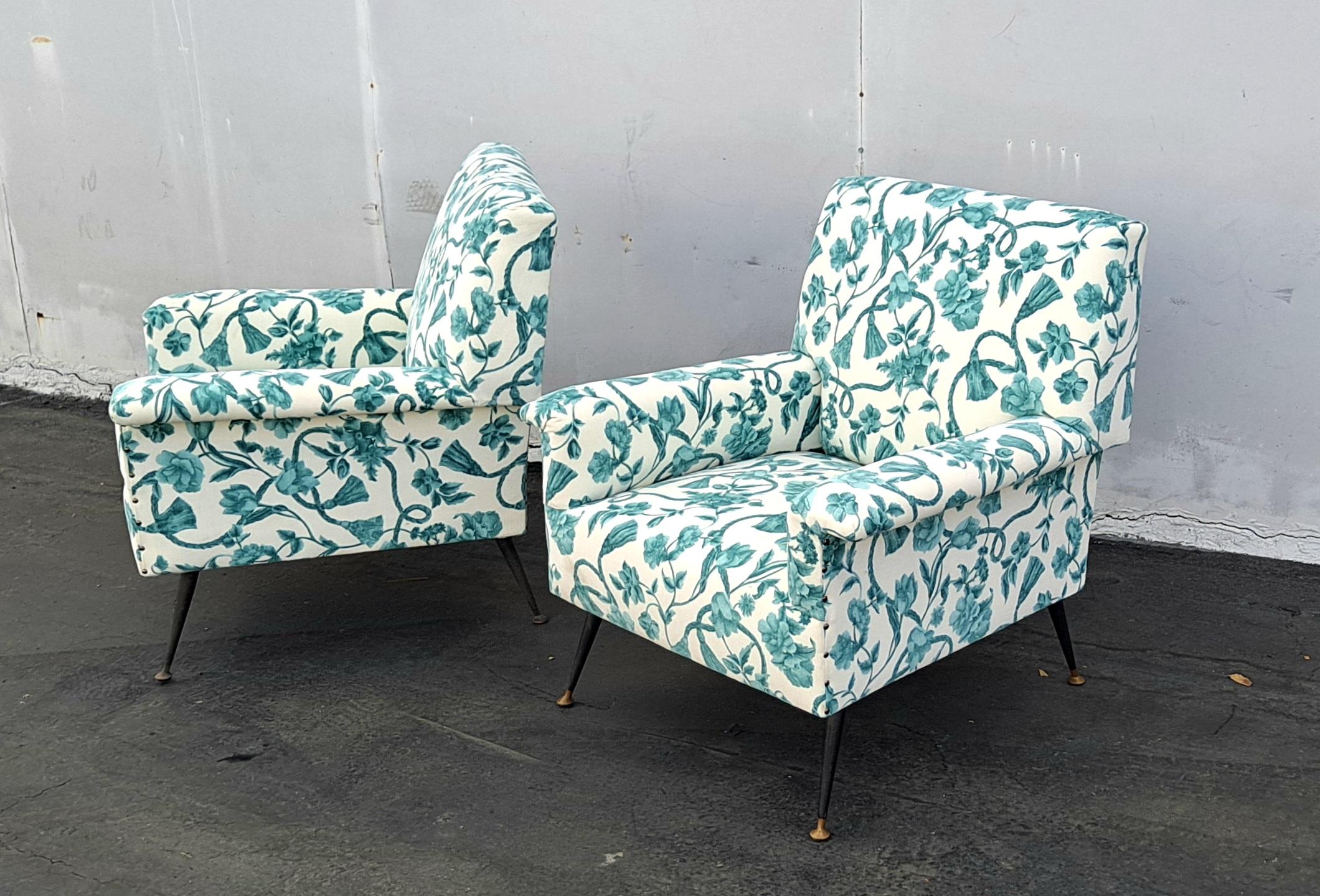 Pair of 1960s armchairs with slightly reclining  armrests, padded with foam and upholstered in new fabric panted black metal legs with brass feet.