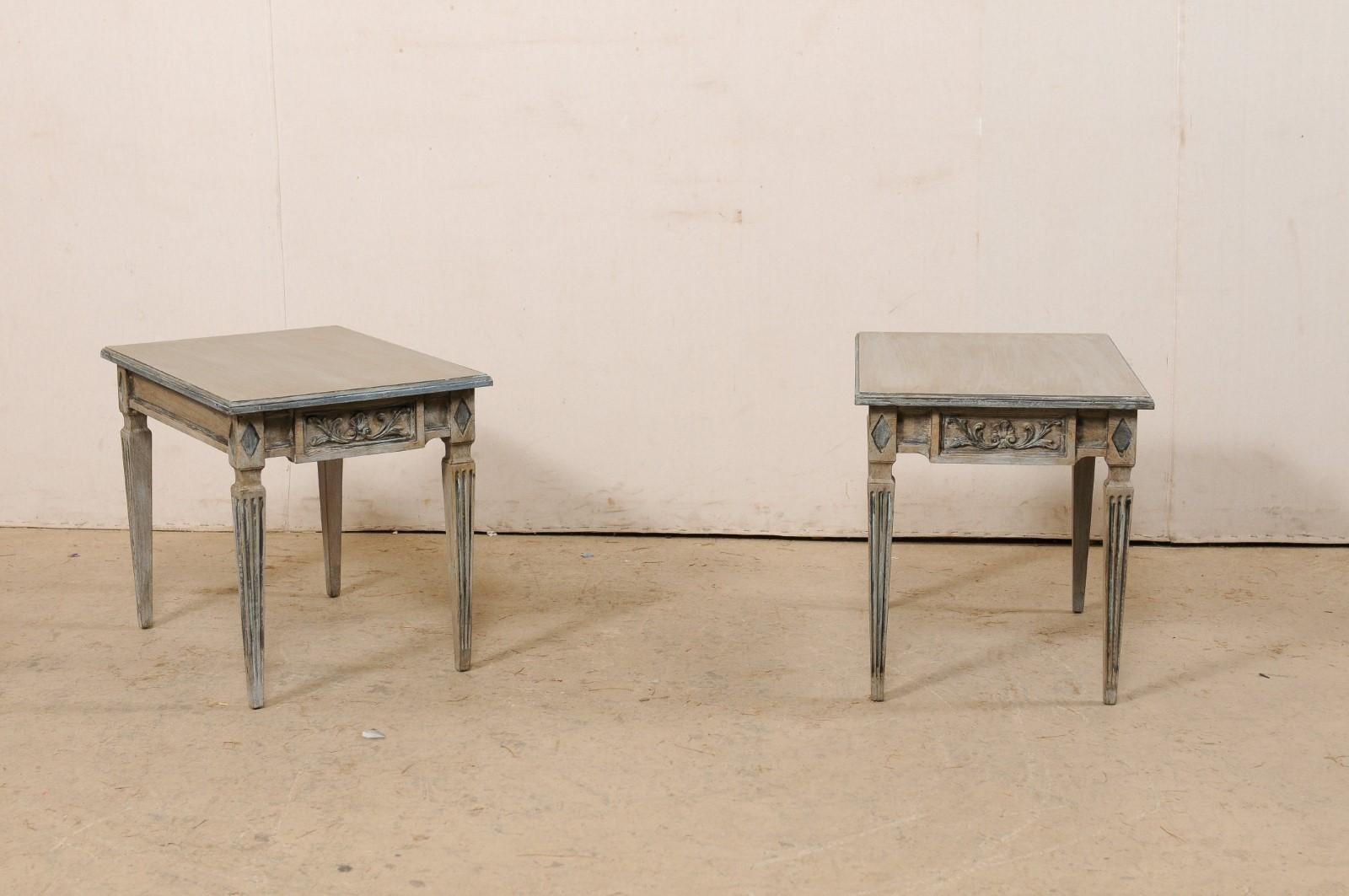 An Italian pair of carved and painted wood side tables. This vintage pair of tables from Italy each have rectangular-shaped tops, which overhang an apron below cared with diamond accents above the legs at each corner, and emphasis on a drop down