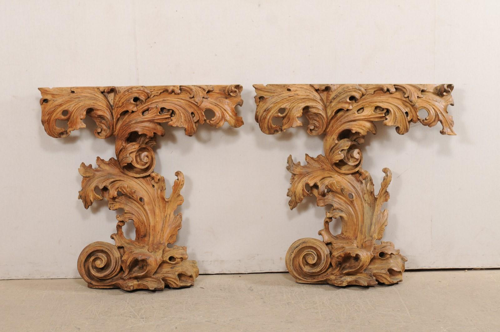 An Italian pair of ornately carved-wood and wall-mounted console tables. This pair of vintage tables from Italy are designed in an elaborate display of scrolling acanthus leaves and volutes. These tables have an elongated rectangular-shaped top,