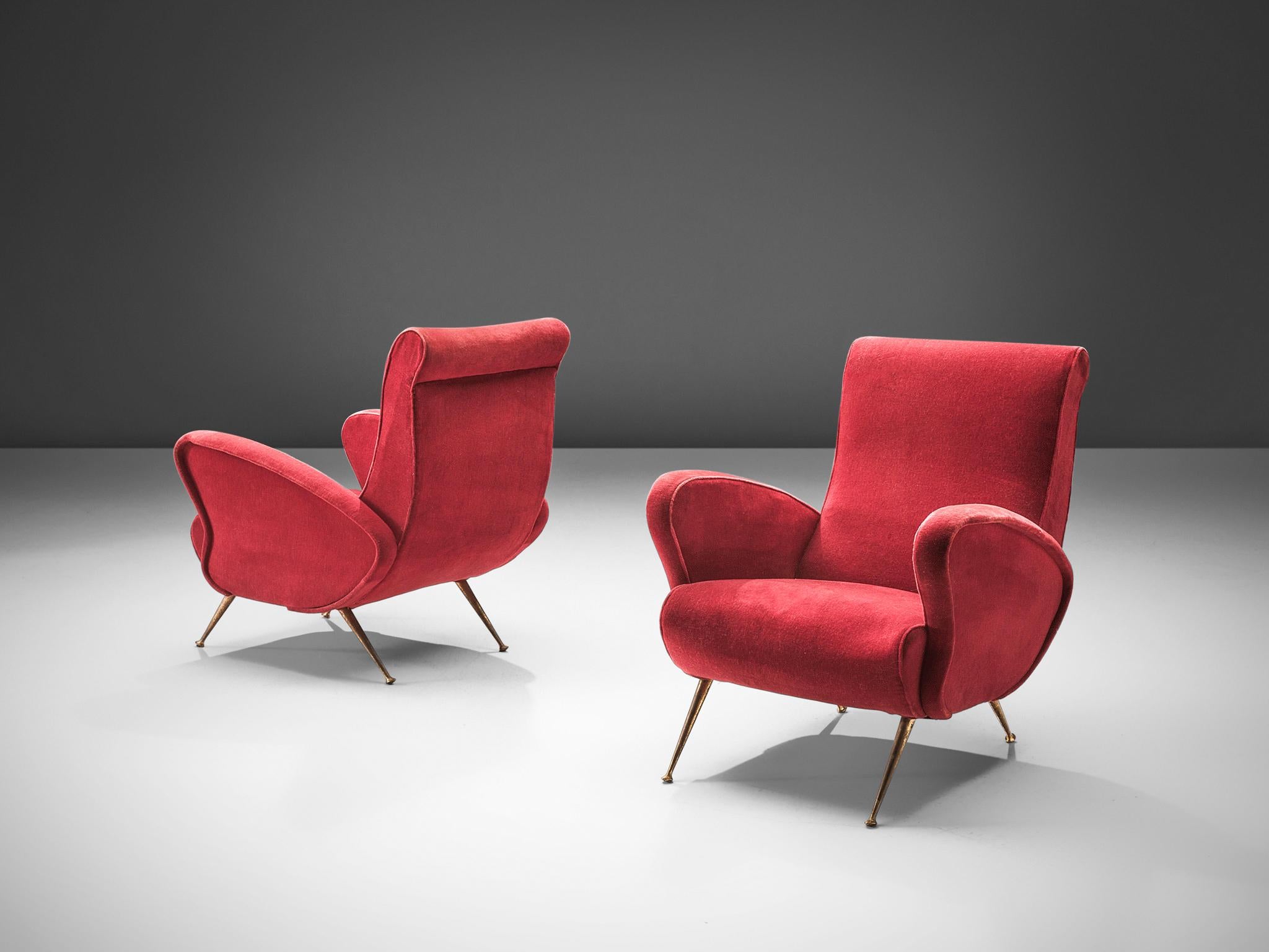 Pair of easy chairs, red velvet, brass, Italy, 1950s.

This pair of lounge chairs is an iconic example of Italian design from the fifties. Organic and sculptural the armchairs are anything but minimalistic. Equipped with the original stiletto brass