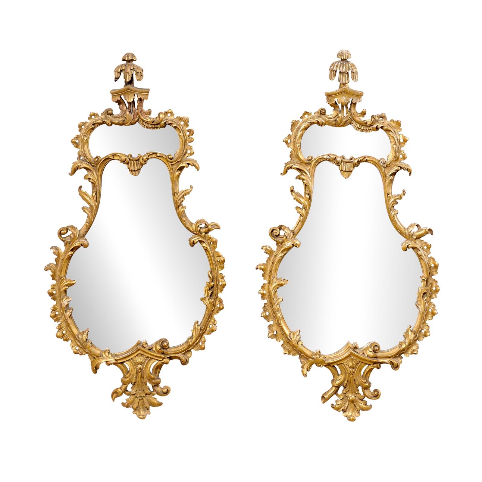 An Italian pair of carved and gilt decorative wall mirrors from the mid 20th century. These vintage mirrors from Italy have shapely-carved, acanthus motif surrounds with beautifully adorn top crests which project outwardly, suspended above the