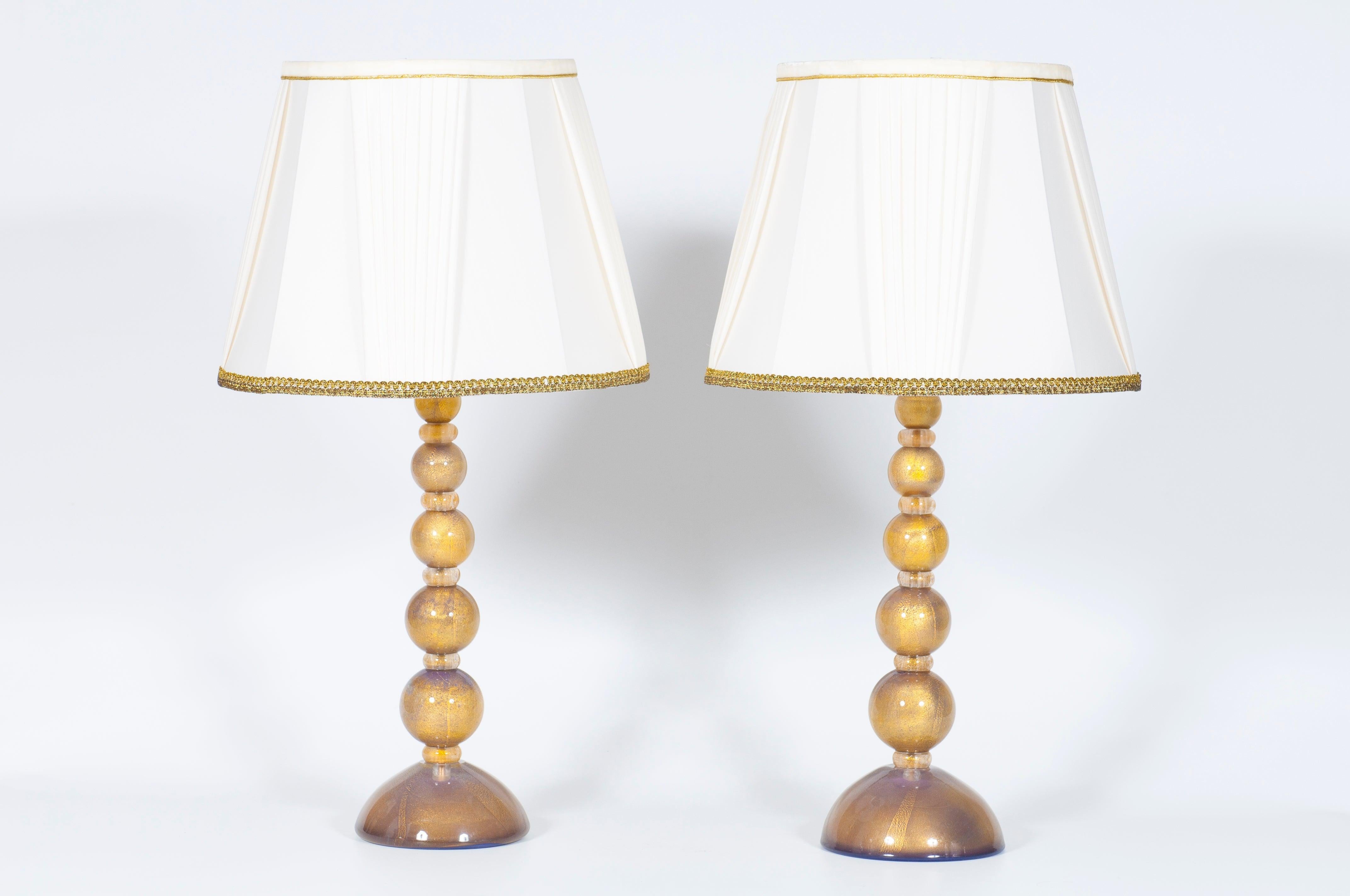 Paire de lampes de table exquises en verre de Murano avec des accents violets et dorés, design italien des années 2000.
Cette exceptionnelle paire de lampes de table, entièrement fabriquée à la main en verre soufflé de Murano, incarne l'art et