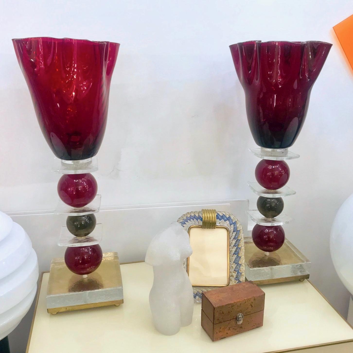 A charming pair of tall lamps in Murano glass, the blown red textured tops with a flowering shape are supported by a stem with three glass spheres in red and olive grey colors, on a clear glass square resting on a handcrafted bronze base raised on