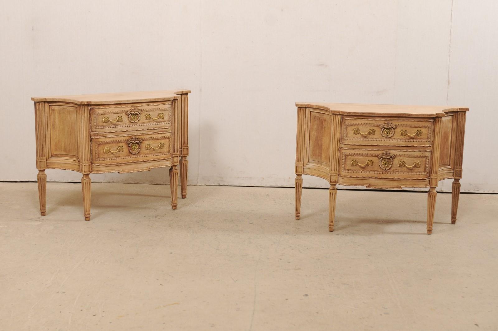 An Italian pair of bleached wood two-drawer chests, neoclassical in style. This vintage pair of raised chests from Italy each feature an elongated backside with shorter front, and graceful concave-scalloped sides, which lends these pieces to also