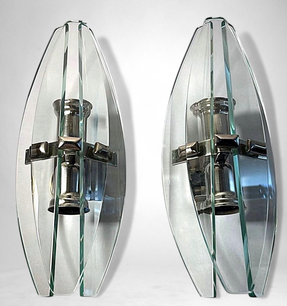 Elegant and linear pair of vintage Italian wall sconces. Each piece features a solid chrome-plated metal frame supporting three finely shaped tempered crystal slabs: one overlapping the other two, creating a refined and dynamic design. The metal