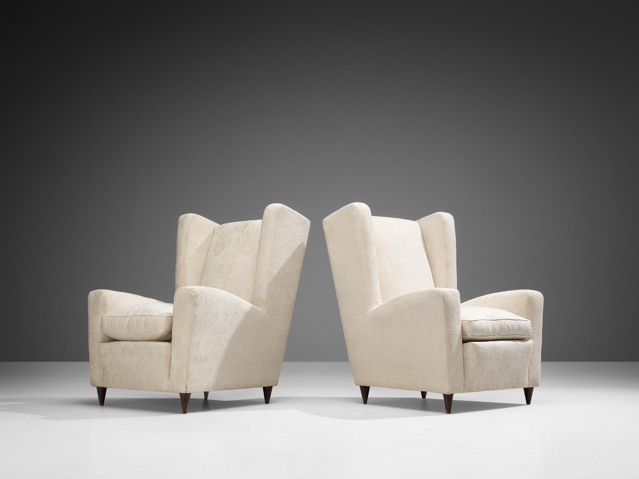 Pair of lounge chairs, fabric, wood, Italy, 1950s.

This Classic Italian Postwar wingback chair has an unusually high back and gracious wings that contain dramatized pointed corners. The armrests feature the same pronounced curves that give the