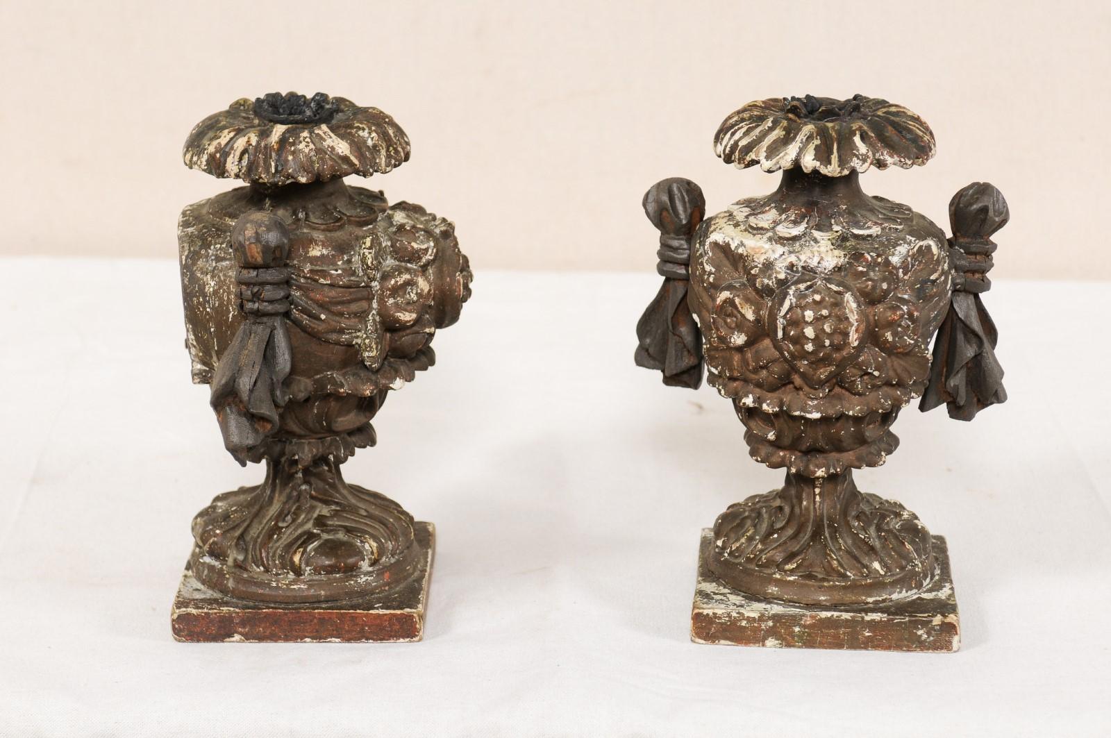 An Italian pair of smaller sized carved-wood candleholders from the early 19th century. These antique candleholders from Italy feature hand carved urn-shaped fragments with floral embellishments, petal leaf upper lips, and handles which give the