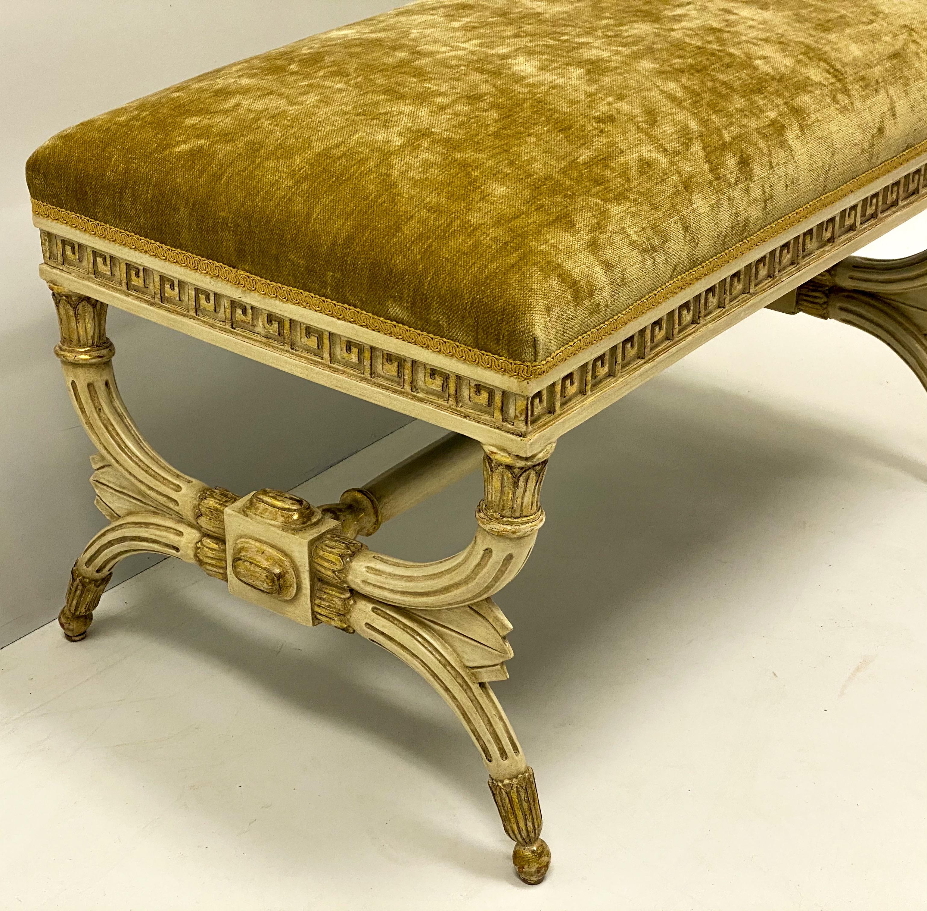 This is a mid-century Italian parcel gilt neo-classical style painted bench. The gold velvet is vintage and shows lite wear. The carved Greek key apron is wonderful. It is unmarked.