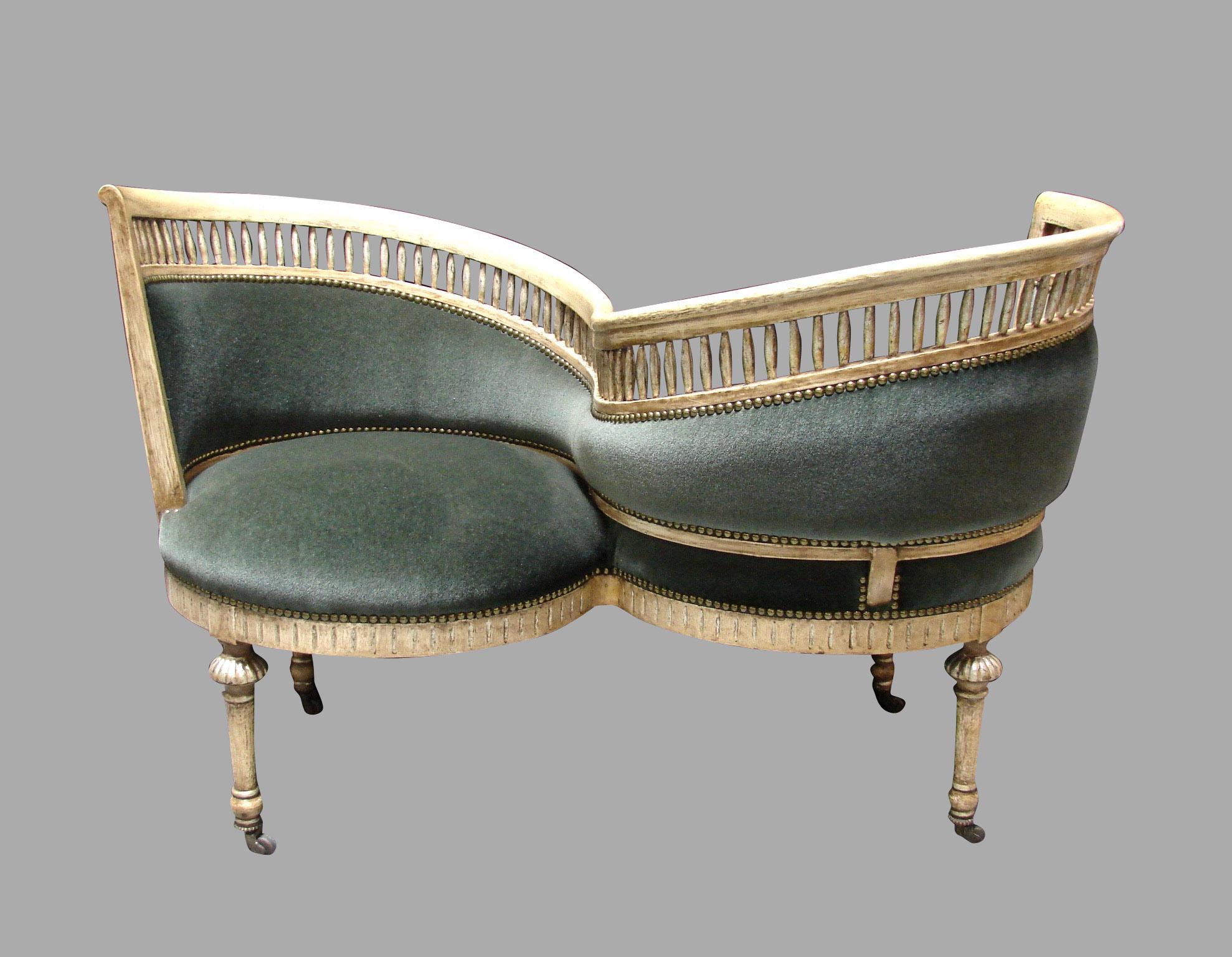 An elegant Italian parcel-gilt cream paint decorated serpentine form sociale or tete a tete, the spindle form top rail over a greyish green mohair upholstered back and seat, finished with nailhead trim over a carved seat rail supported on round