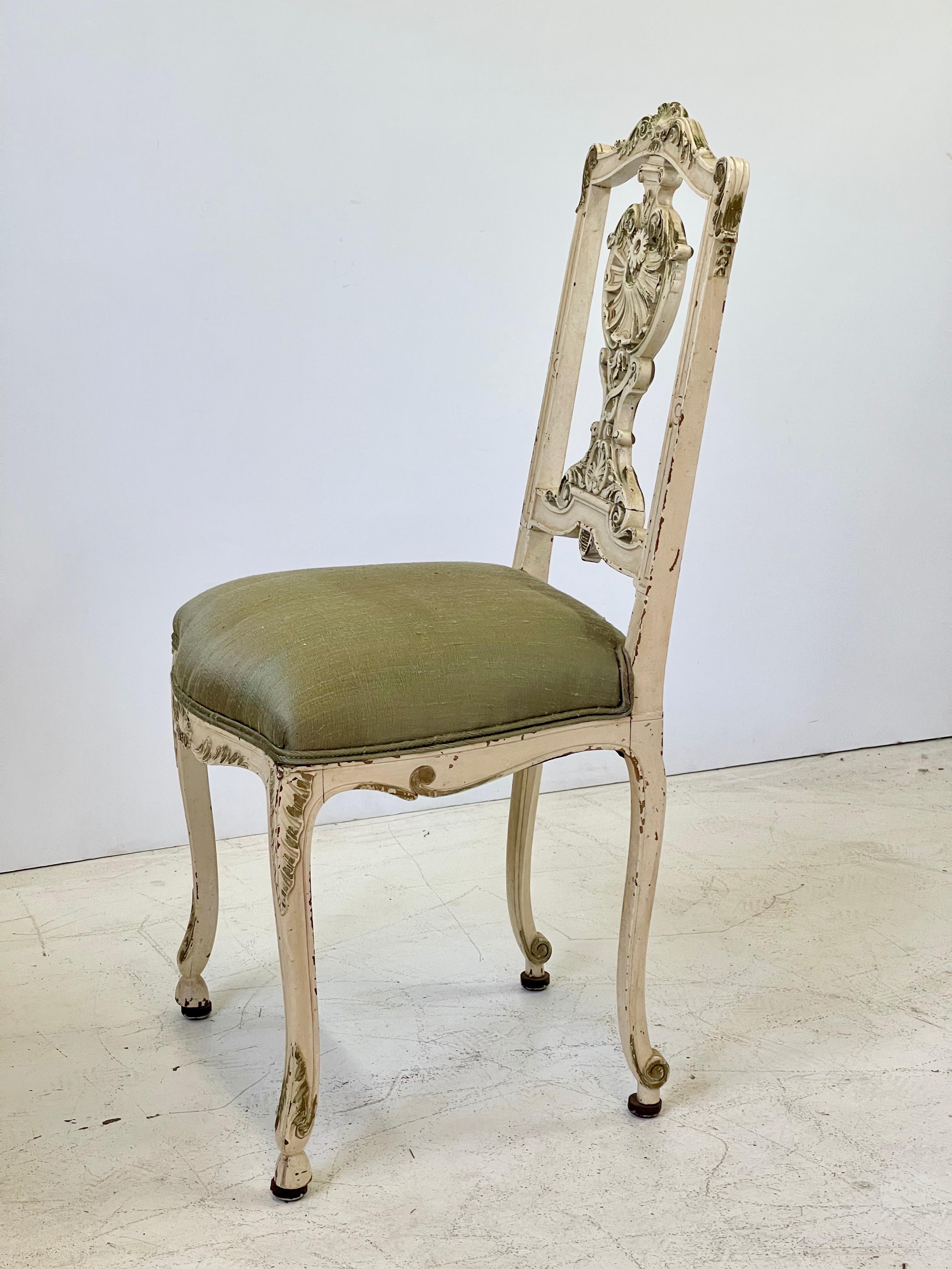 Early 20th century Italian vanity or petite side chair finely carved in the Louis XV style. The chair is painted in cream with gilded details that have beautifully worn over time. The seat has been newly upholstered in a complimentary green raw silk.