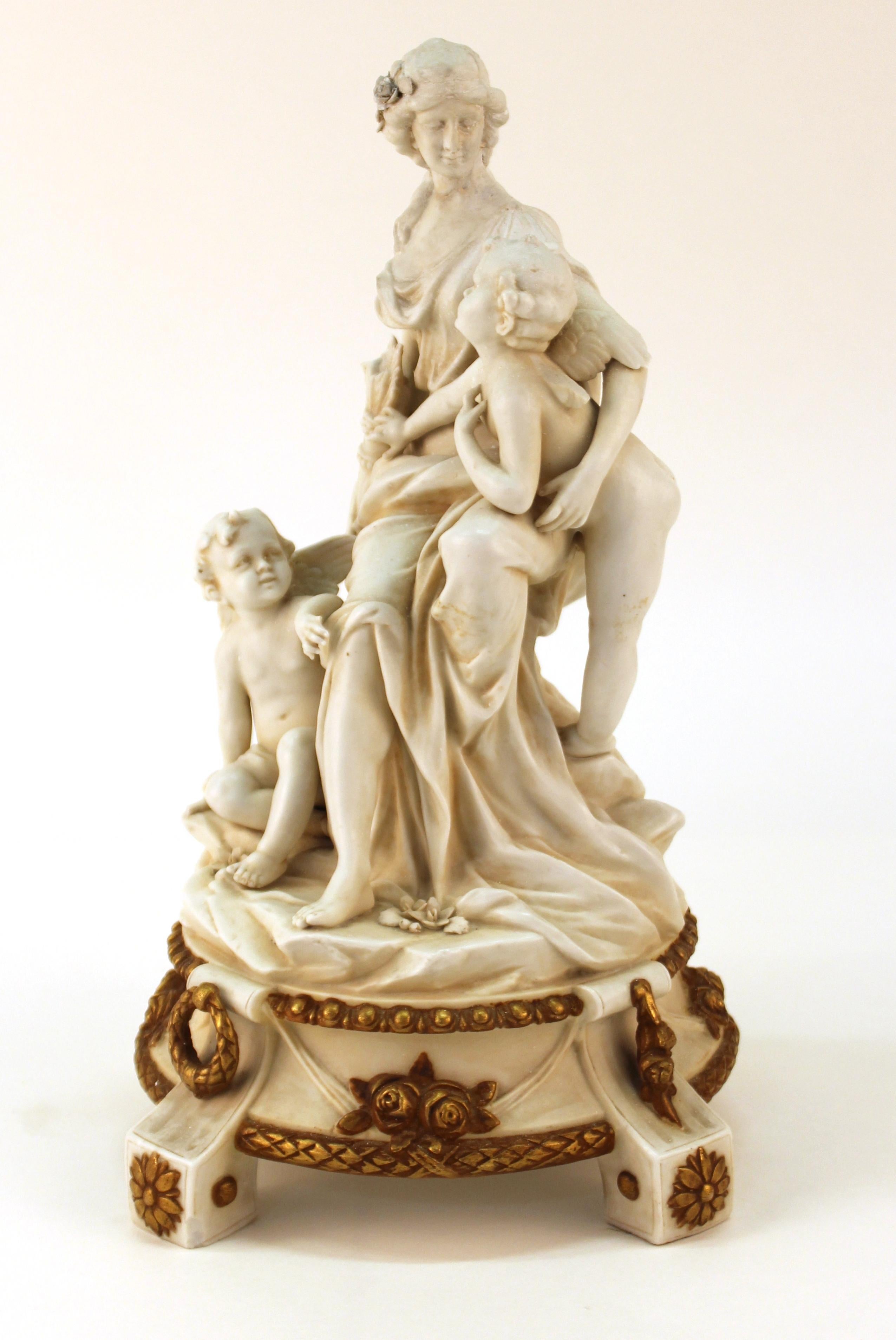 Parianware figurine, probably 19th century, of a seated Venus with two cherubs, the goddess teasingly holding one's quiver of arrows out of reach. The piece has a circular base with gilt-painted ring handles, rosettes, roses, and laurel leaf edges.