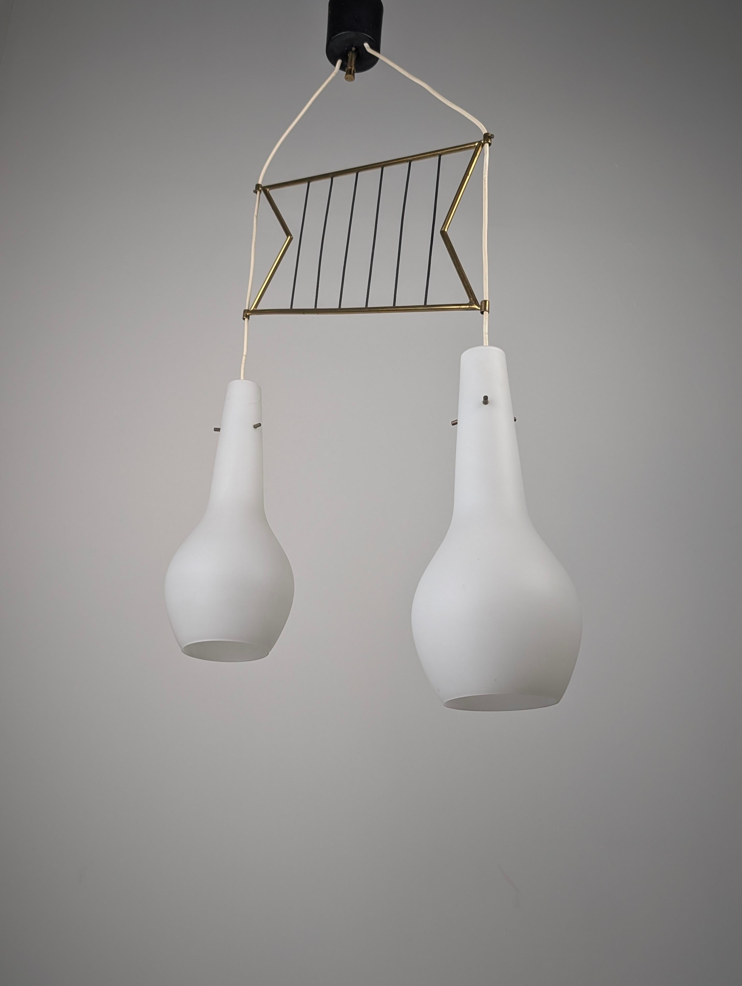 Italian ceiling lamp from the 1950s with a geometric brass frame and black rods, holding two blown opaline glass shades suspended at different heights. The design balances linear structure with soft glass forms, producing warm and even lighting. The