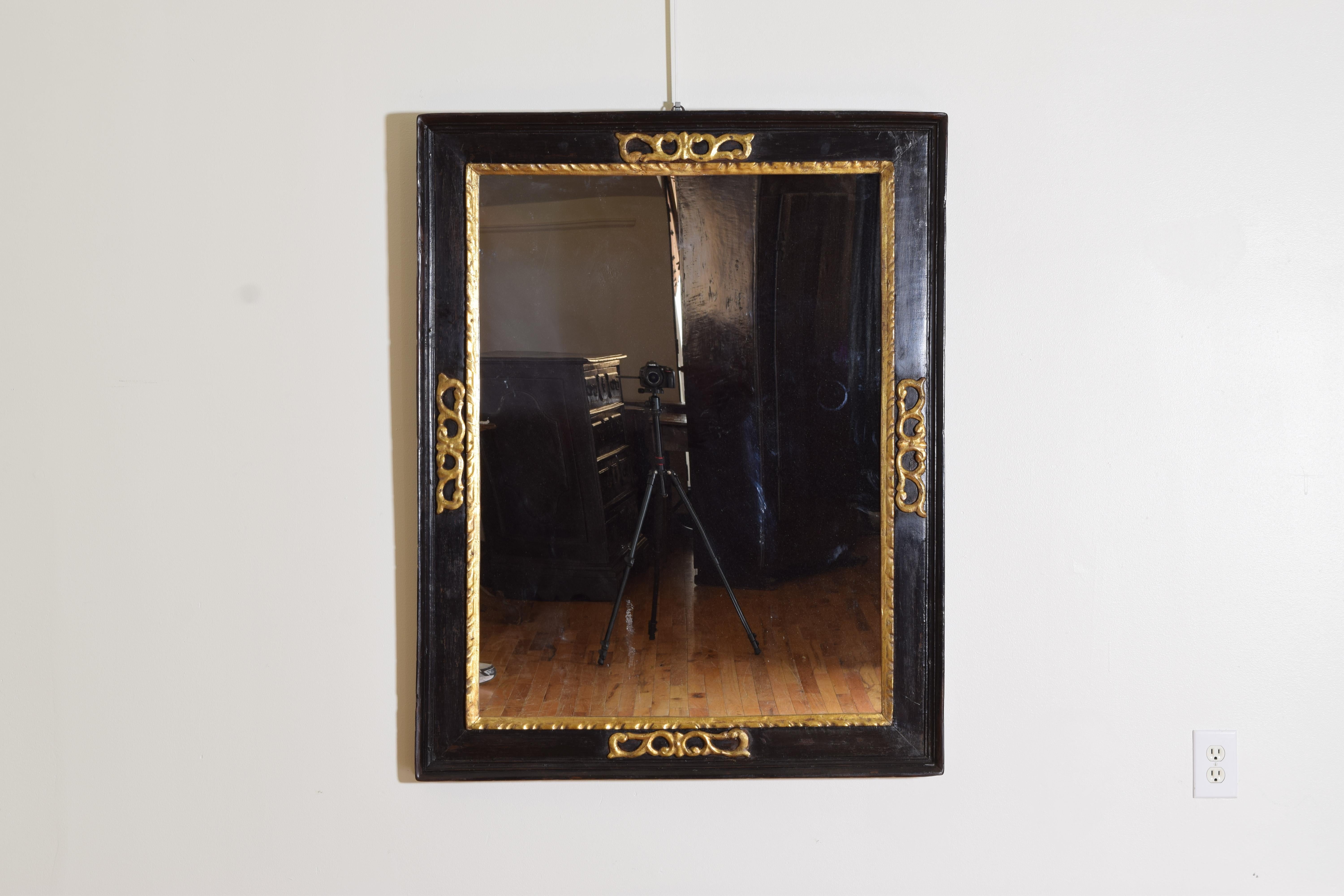 The rectangular ebonized frame having an outer molded edge, the interior adorned with giltwood carvings in circular scroll forms, the inner molding also giltwood, mirror plate is modern.